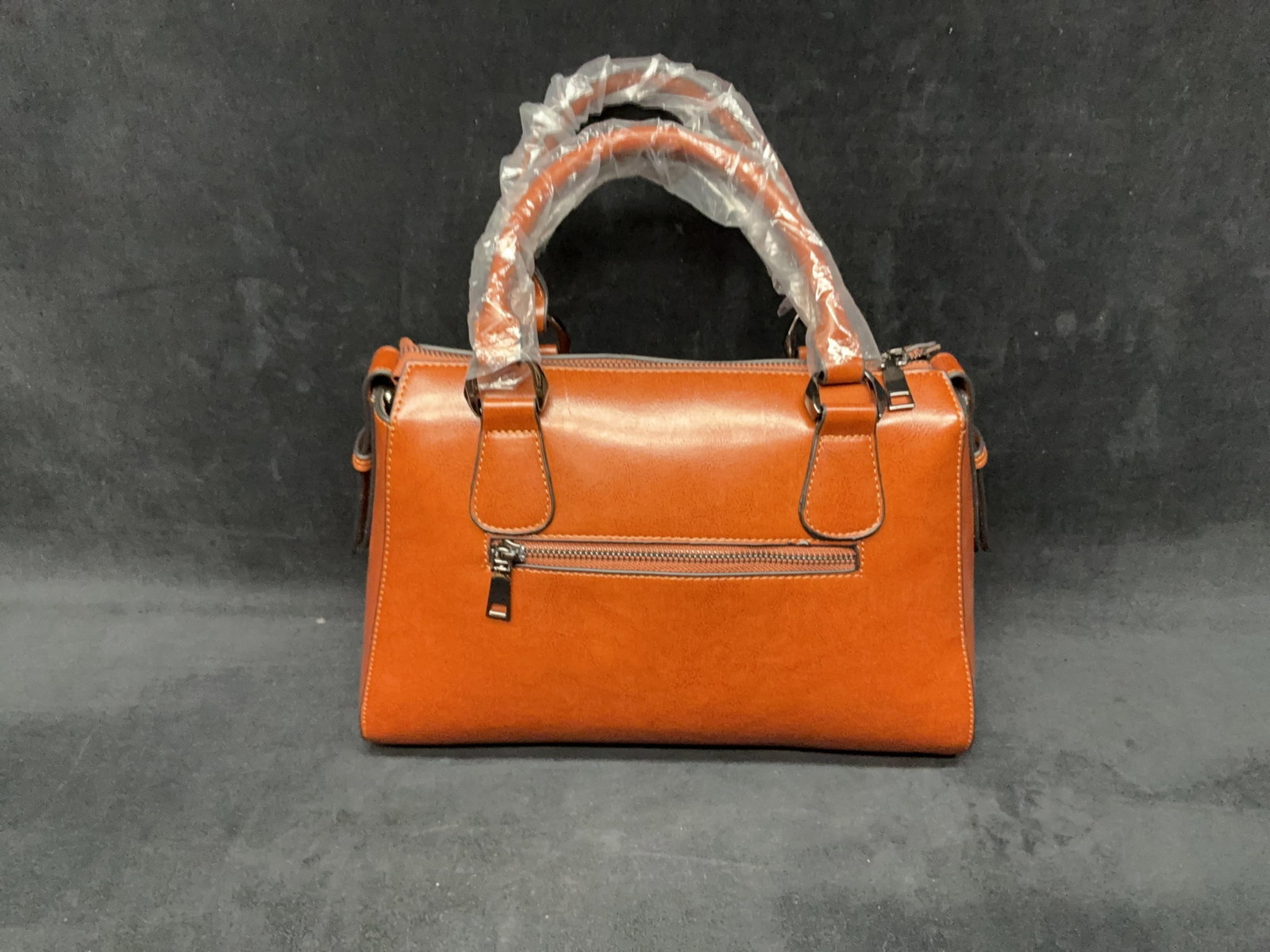 Brown Leather-Style Satchel Handbag: Brown leather-style satchel handbag with black trim, top handles, and detachable shoulder strap. Appears unused with protective wrapping present on handles. Please see photos for best