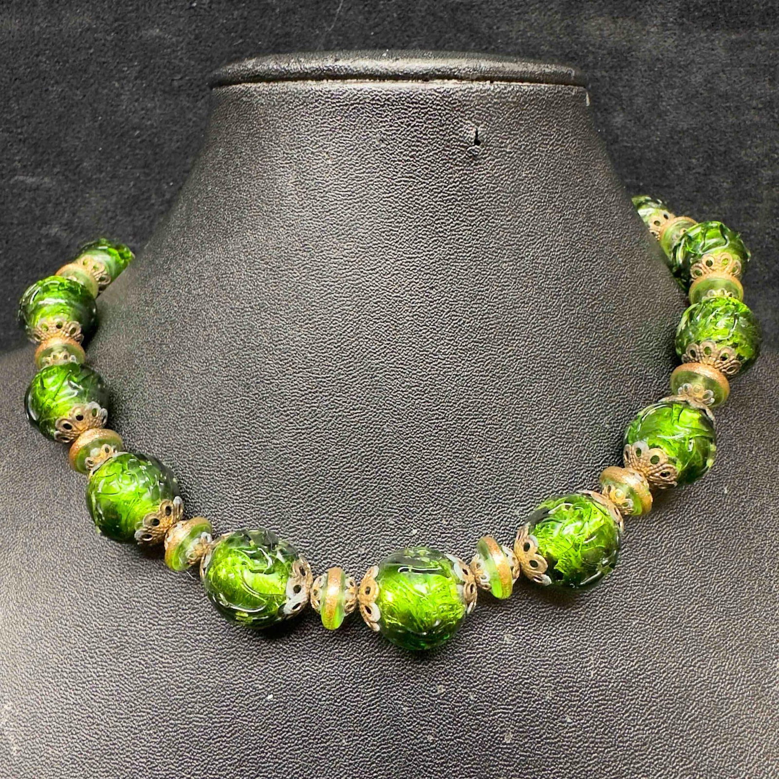 Murano Venetian Lamp Work Art Glass Dark Green Beaded Necklace C73: Murano Venetian Lamp Work Art Glass Dark Green Beaded Necklace C73. Necklace with green glass beads with beautiful designs on each. The necklace features gold accents. The necklace features a barrel