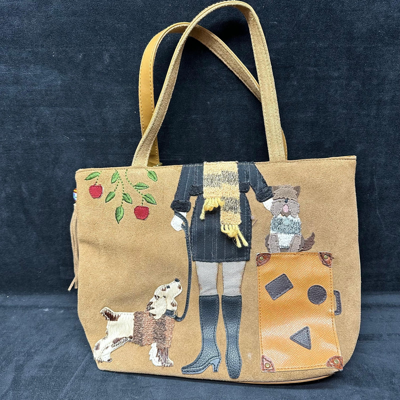 St Johns Bay Brown Suede Tote Handbag with Dog and Girl Applique: Brown/Tan suede tote bag featuring stitched applique of a girl with two dogs and a suitcase motif on the front. Includes dual shoulder straps, an interior zipper compartment, slip pockets, and a 