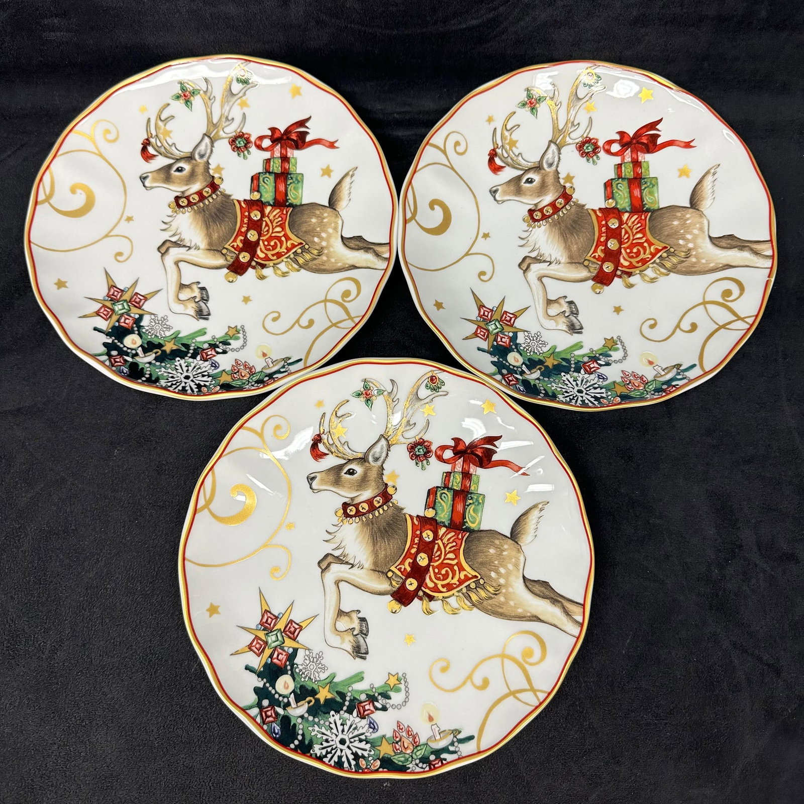 Set of 3 Williams Sonoma Christmas Reindeer Salad Plates: Set of three Williams-Sonoma holiday salad plates featuring a leaping reindeer with an ornate red saddle, holiday accents, and wrapped gifts on its back. Gold scroll work, festive stars, and