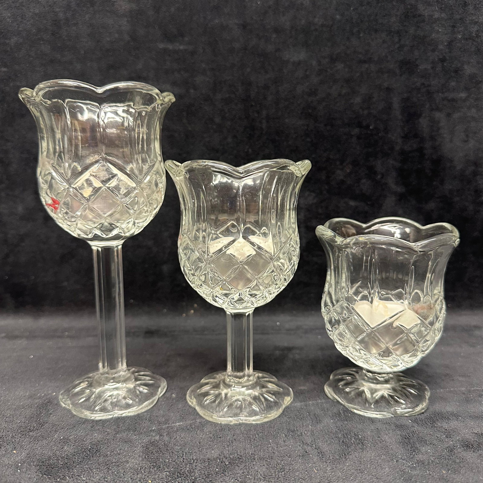 Set of Three Clear Pressed Glass Tulip Form Candle Holders: Group of three clear pressed glass candle holders in a tulip form design with scalloped rims and paneled stems. Each example features a diamond-pattern bowl and a round base. Includes tea light candle