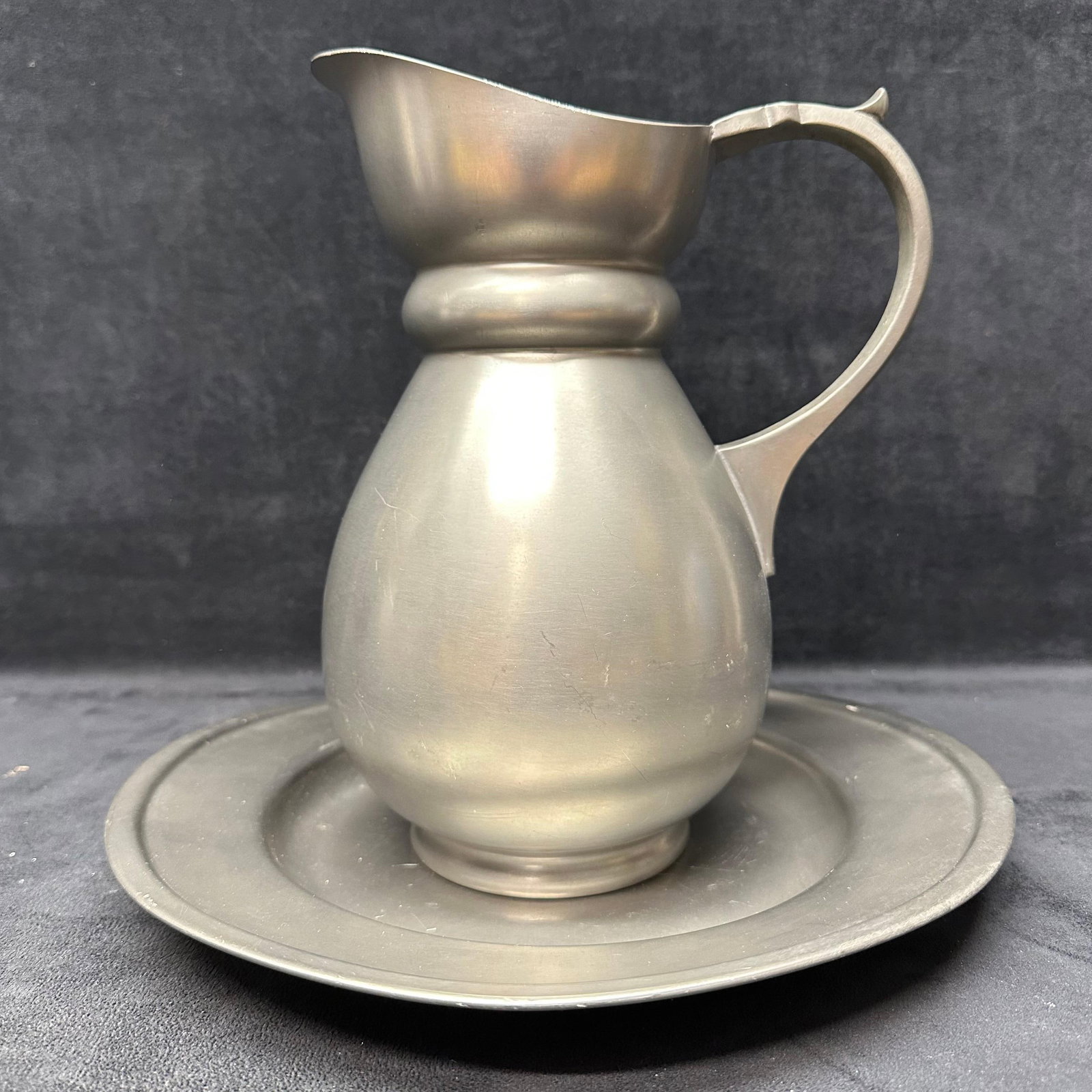Royal Holland Daalderop Pewter Pitcher and Basin Plate Set: Royal Holland Daalderop pewter pitcher and basin set, crafted in Holland from 94% pure tin (Sn). This elegant two-piece set features smooth, rounded lines with a soft satin finish, typical of mid-cent