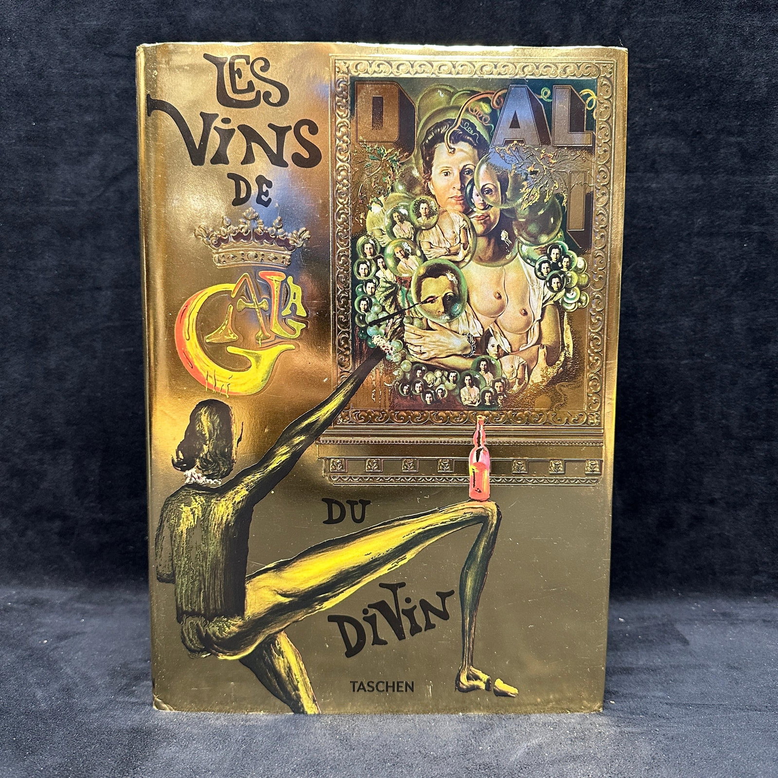 Salvador Dali Les Vins De Gala Taschen Hardcover Book: Hardcover edition of Les Vins De Gala by Salvador Dali published by Taschen. Features surrealist wine-themed artwork, text, and illustrations throughout with metallic dust jacket. Includes handwritten