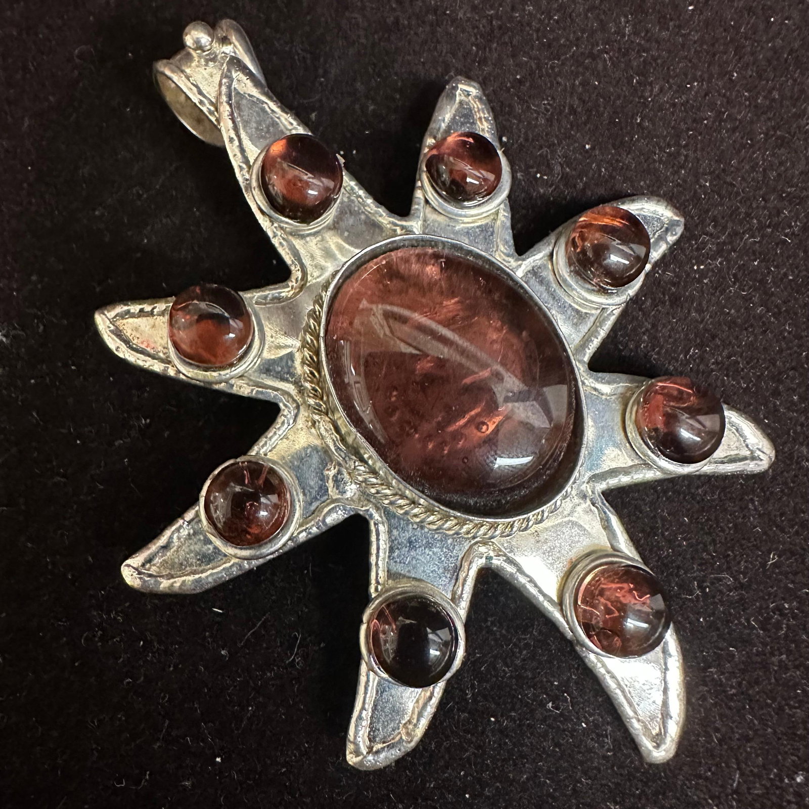 Silver Tone Sunburst Pendant with Red Purple Hue Glass Cabochons: Large silver-tone sunburst pendant set with an oval red-purple hue glass cabochon at the center surrounded by eight matching round cabochons. Bold sculptural rays with hammered back and fixed bail. Ba