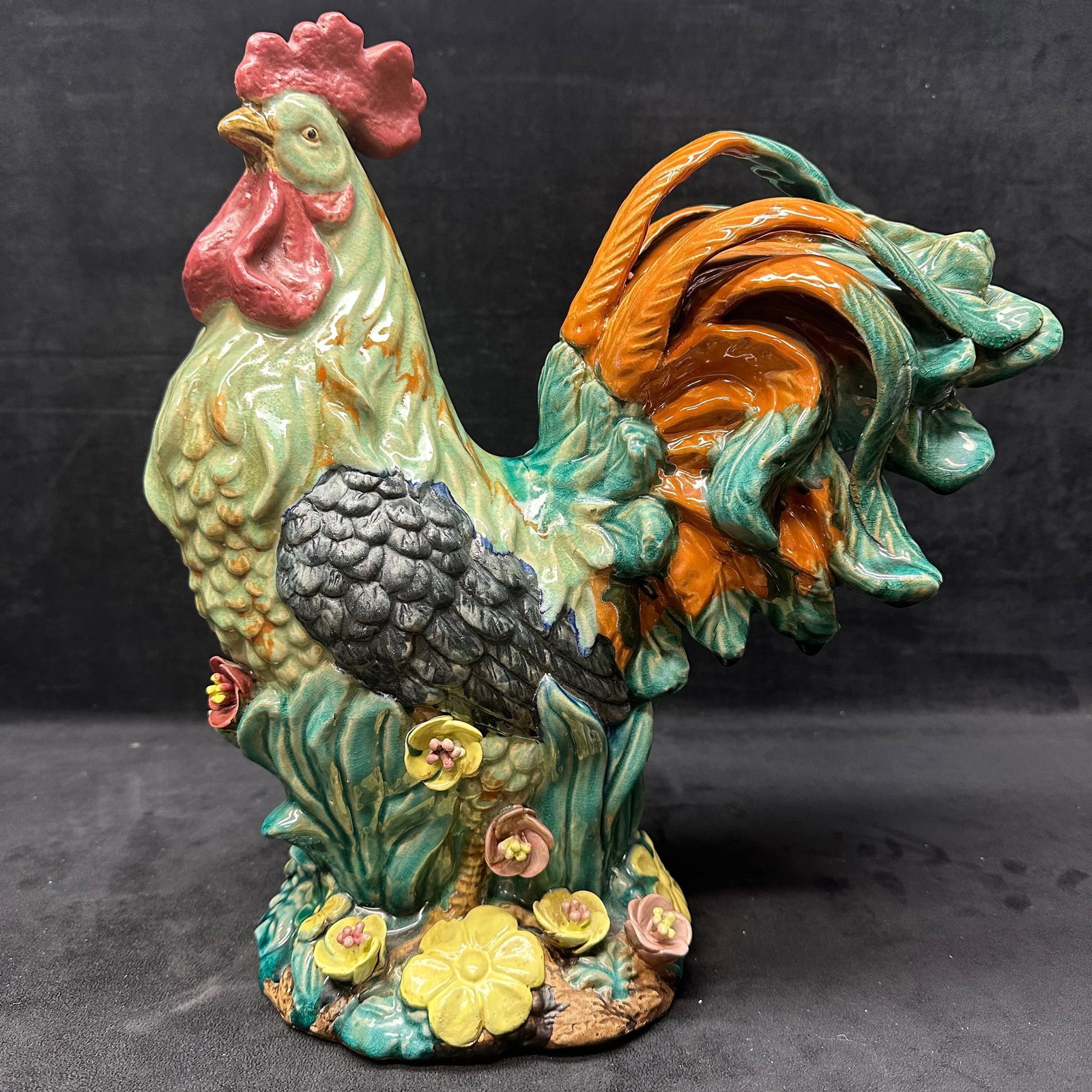 Large Hand Painted Ceramic Rooster Figurine with Floral Base: Large decorative ceramic rooster figurine with hand-painted details. Features a green and teal body, orange and teal tail feathers, red comb and wattle, and textured feather detailing. The rooster