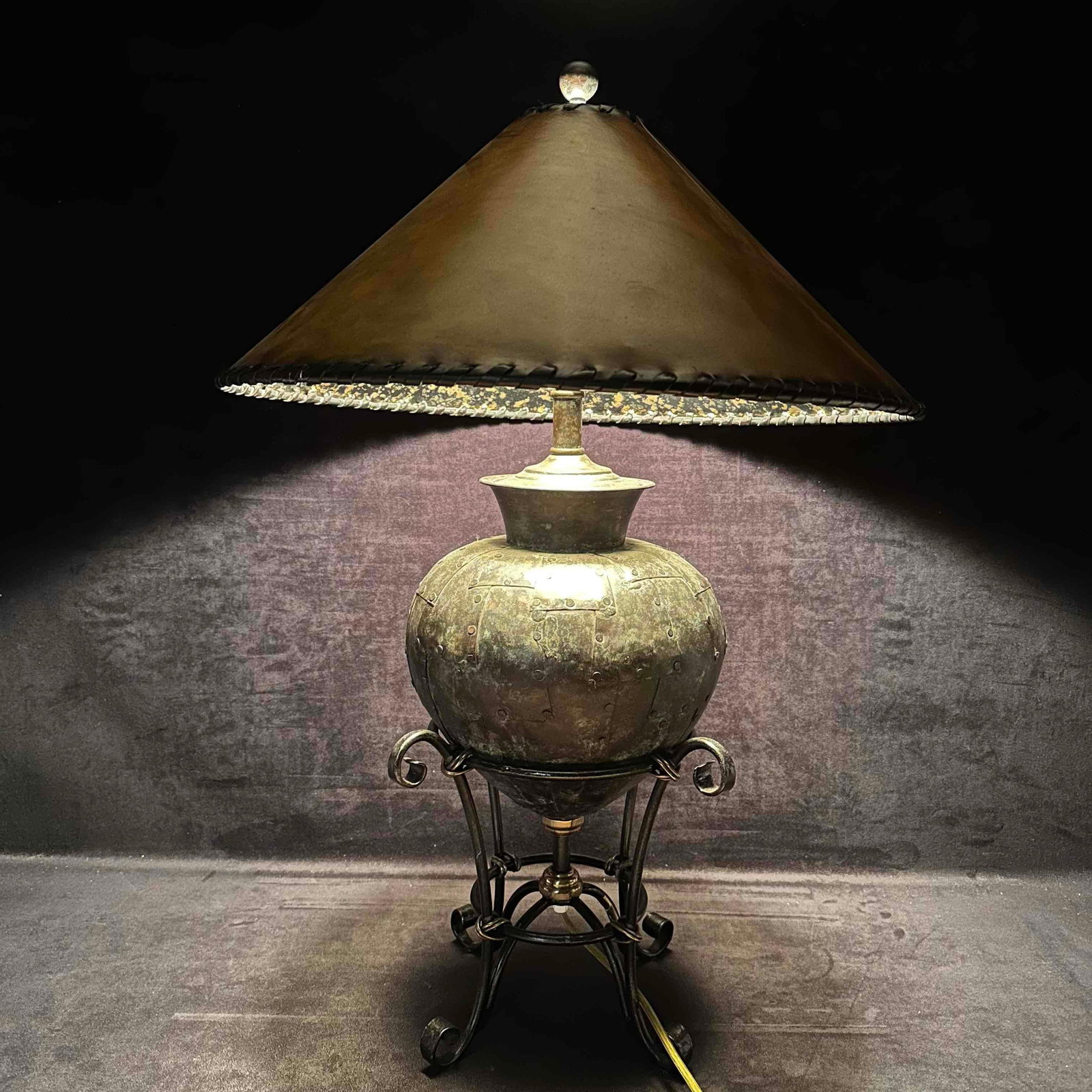 Maitland Smith Lamp Interwoven Leather Shade and Rustic Metal Base Home Decor: This Maitland Smith is topped with a conical or pyramidal shade made of a material appearing to be aged leather giving it a rustic style. The metal urn-shaped body base resting on wrought-iron-style s
