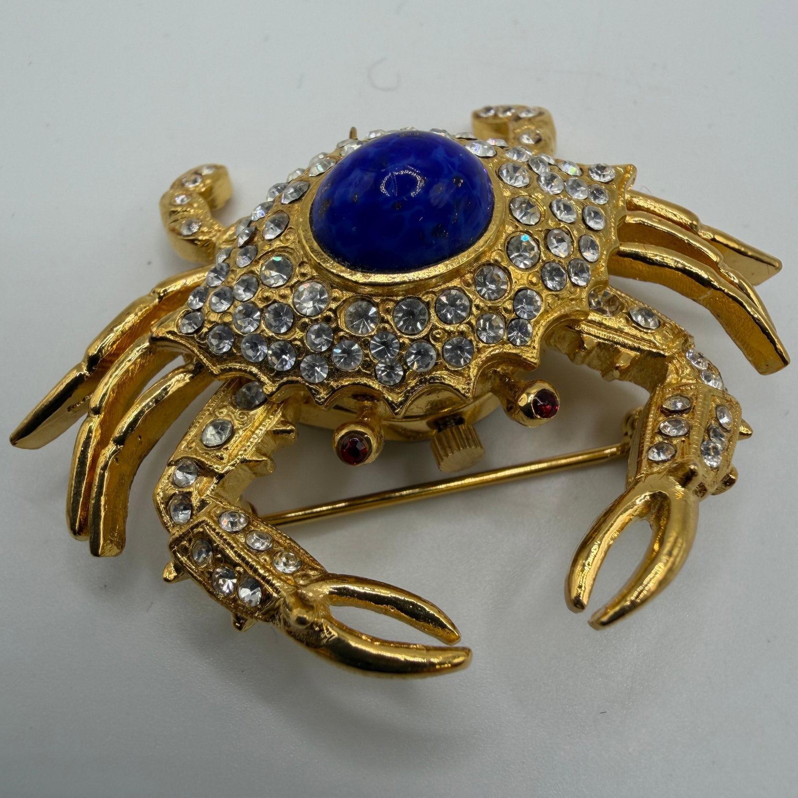 Kenneth Jay Lane Lapis Clear and Red Rhinestone Crab Watch KJL Brooch: KJL Kenneth Jay Lane brooch ocean-inspired piece crafted in a gold-tone metal. The detailed crab design features an oval blue lapis cabochon, clear rhinestone-encrusted shell, and red rhinestone eyes.