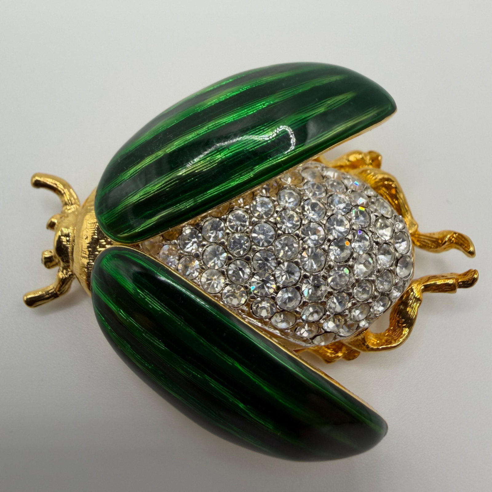 Kenneth Jay Lane KJL Green Enamel and Crystal Beetle Insect Brooch: Kenneth Jay Lane (KJL) designer retractable beetle bug insect brooch featuring translucent emerald green enamel wings that open to reveal a pave-set clear crystal body. Finished in gold-tone metal wit
