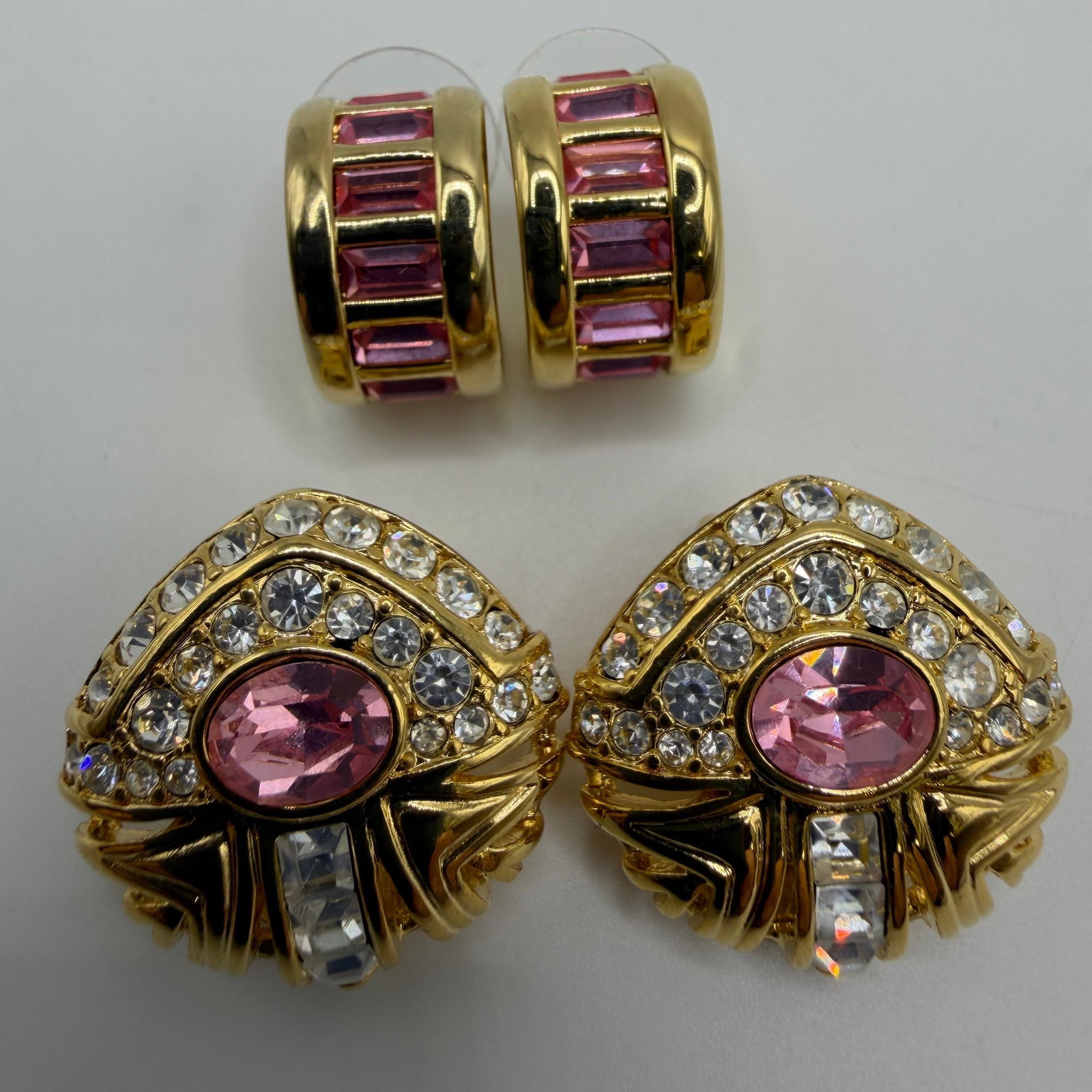Nolan Miller Pink Crystal Costume Earrings HG26: Group of two pairs of Nolan Miller gold-tone costume earrings. Includes one pair of clip-on earrings featuring pink oval rhinestones accented by clear crystals in an Art Deco-inspired design, and one 