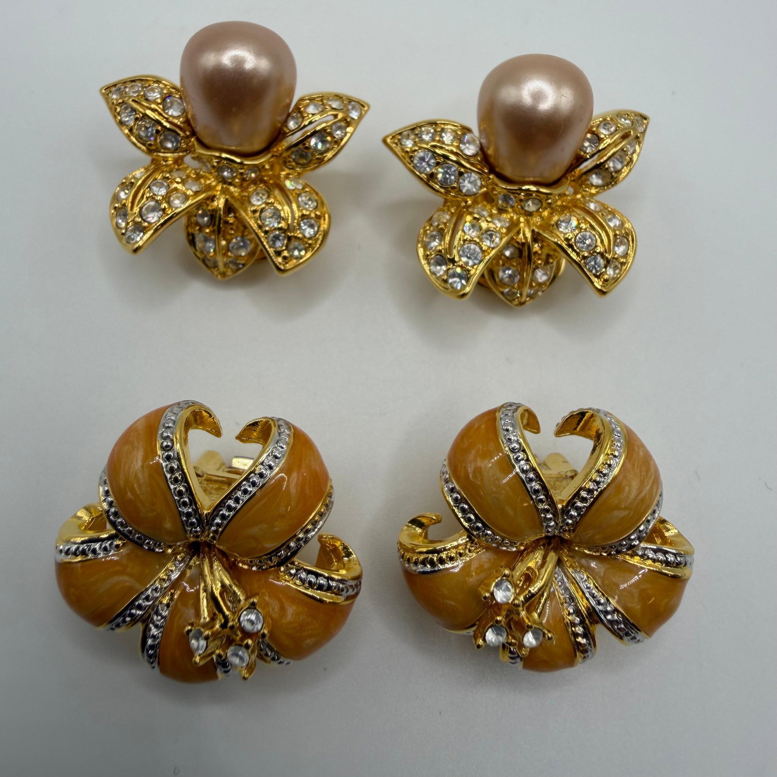 Two Pairs of Nolan Miller Designer Clip-On Earrings Peach Champagne Colored HG28: Collection of two pairs of signed Nolan Miller designer clip-on earrings. Includes a floral-inspired pair with champagne faux pearl centers accented by clear rhinestones in a gold-tone setting, and a