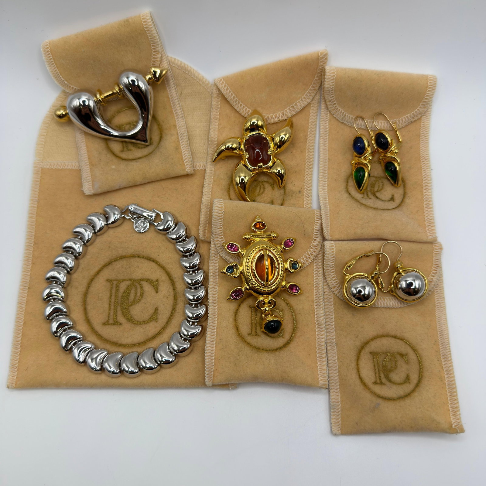 PC Costume Jewelry Collection Bracelet Brooches Earrings Silver Gold Tone: Collection of signed PC costume jewelry including a silver-tone bracelet, two-tone heart brooch, abstract gold-tone brooch with cabochon center, jeweled shield-style brooch with amber-tone and
