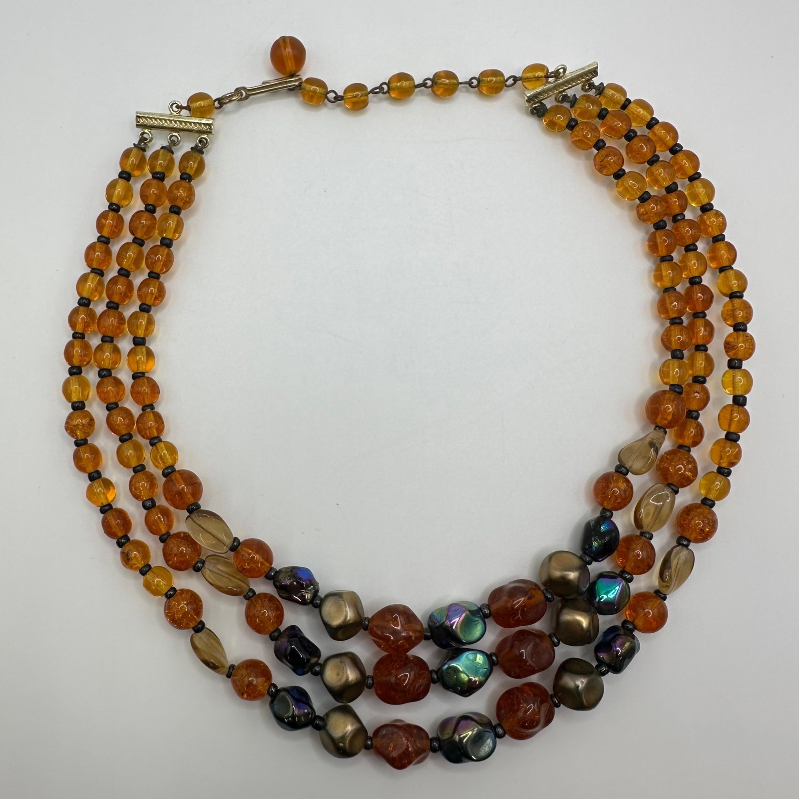 Multi-Strand Natural Amber Resin Iridescent Glass Bead Necklace: Multi-strand necklace featuring graduated round and irregular natural amber beads, likely Baltic amber or amber resin. Accented with iridescent glass beads, a peacock-tone finish, matte metallic-look 
