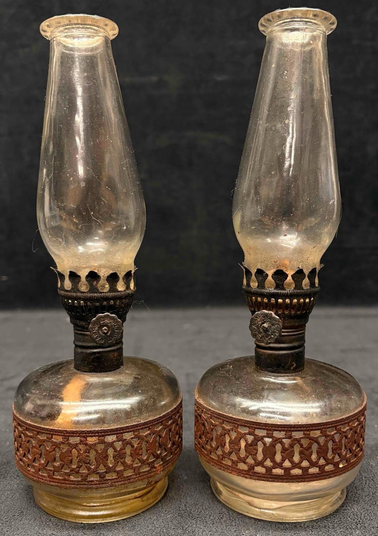 Set of Two 1970s Lamplight Farms Oil Lamp: This lot features a clear glass reservoir with a decorative metal inlay band. These lamps are vintage decorative pieces, suspected to have been manufactured in the 70s. Their age is visible as it
