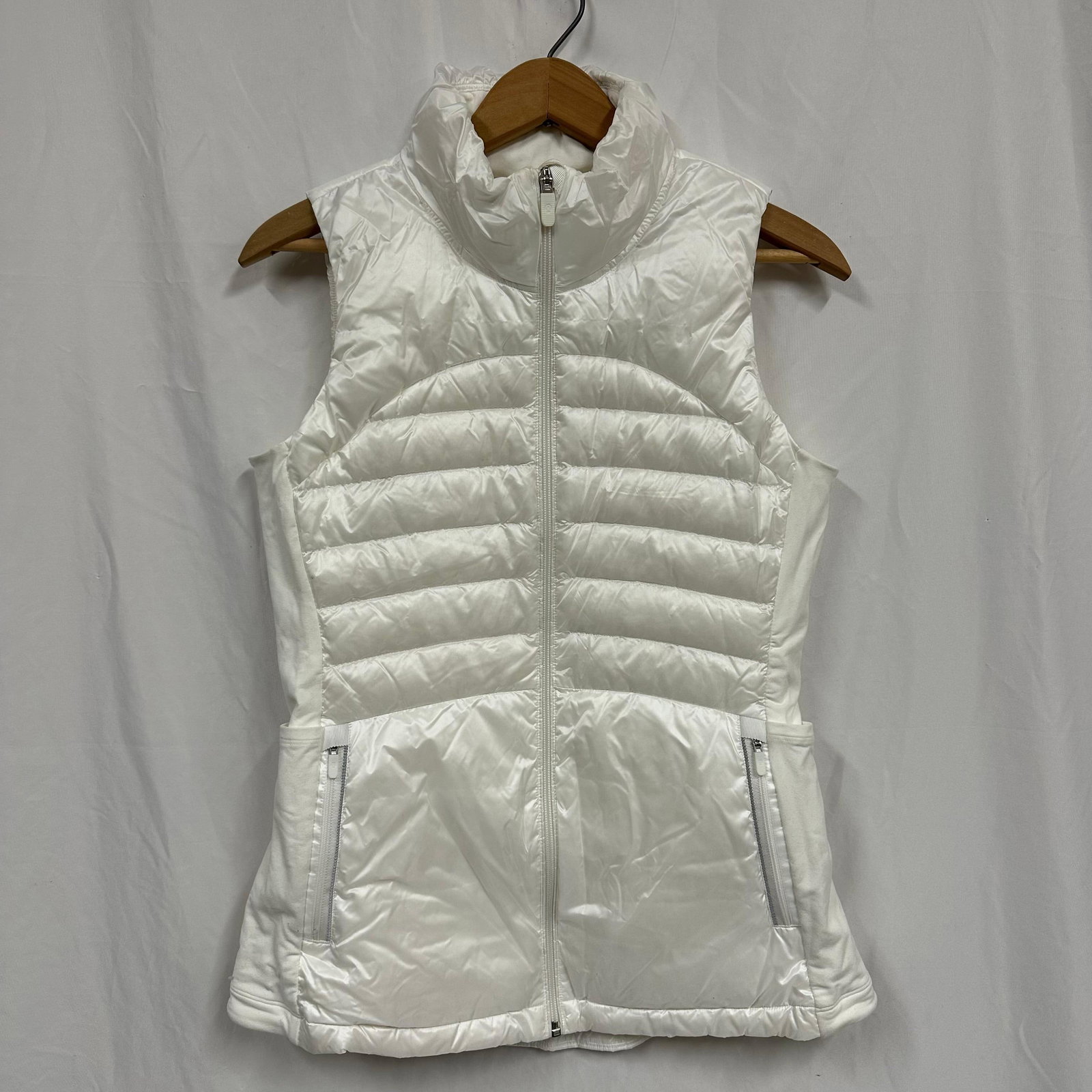 Lululemon Women White Quilted Down Puffer Vest Full Zip: Women’s Lululemon insulated puffer vest in white. Sleeveless, full front zip with stand collar. Quilted nylon body with stretch side panels for a fitted, athletic shape. Two zippered front pocke