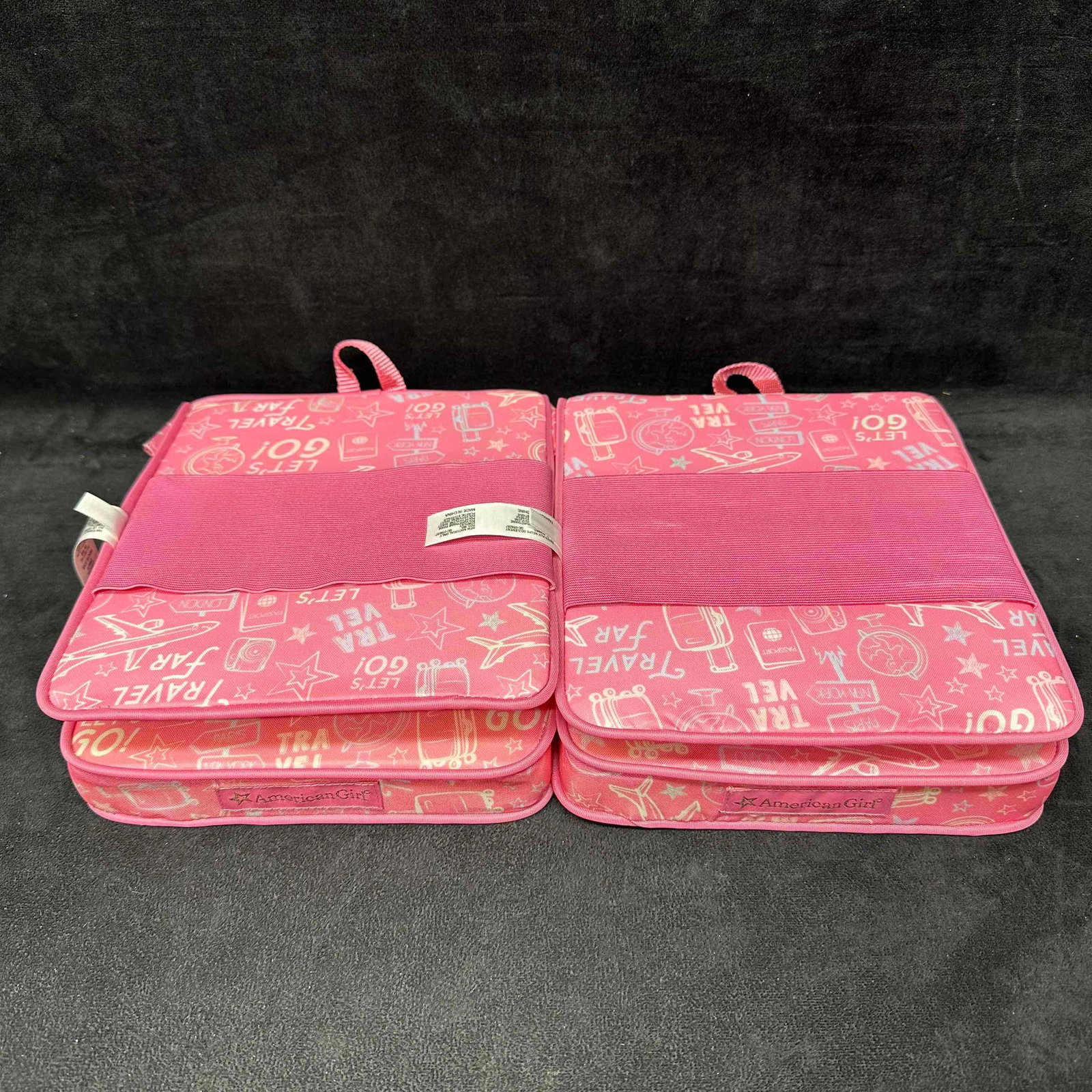 American Girl Doll Pink Love to Travel Seat Chair Set of 2: Pair of American Girl doll travel seats in bright pink with playful “Let’s Go!” and travel-themed designs. Each folds open to create a compact chair setup for dolls and includes