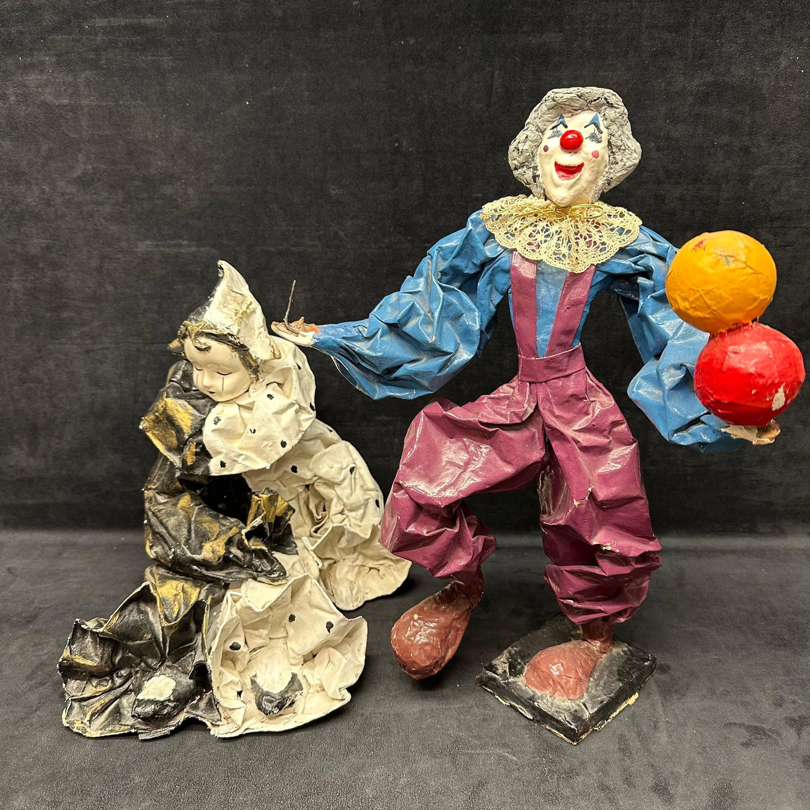 Pair of Papier Mache Clown Figures Mexico: Pair of handmade papier-mache clown sculptures, each with expressive faces and colorful costumes. One depicts a seated clown in black and white polka dots, signed “Calleja,” and