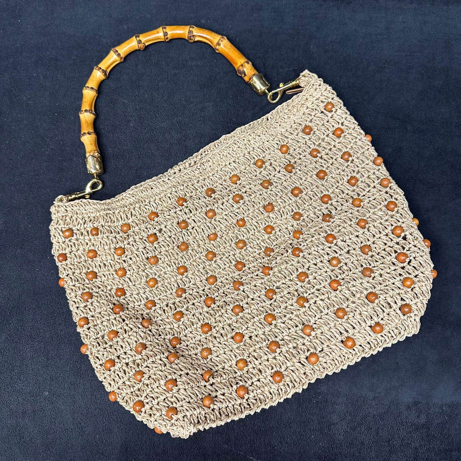 Woven Straw handbag with Wood Bead Accents Bamboo Handle Multi Strap Options: Woven straw-style handbag featuring an allover textured weave accented with small round wood beads. The bag is fitted with a bamboo top handle with metal clasps and includes additional interchangeable