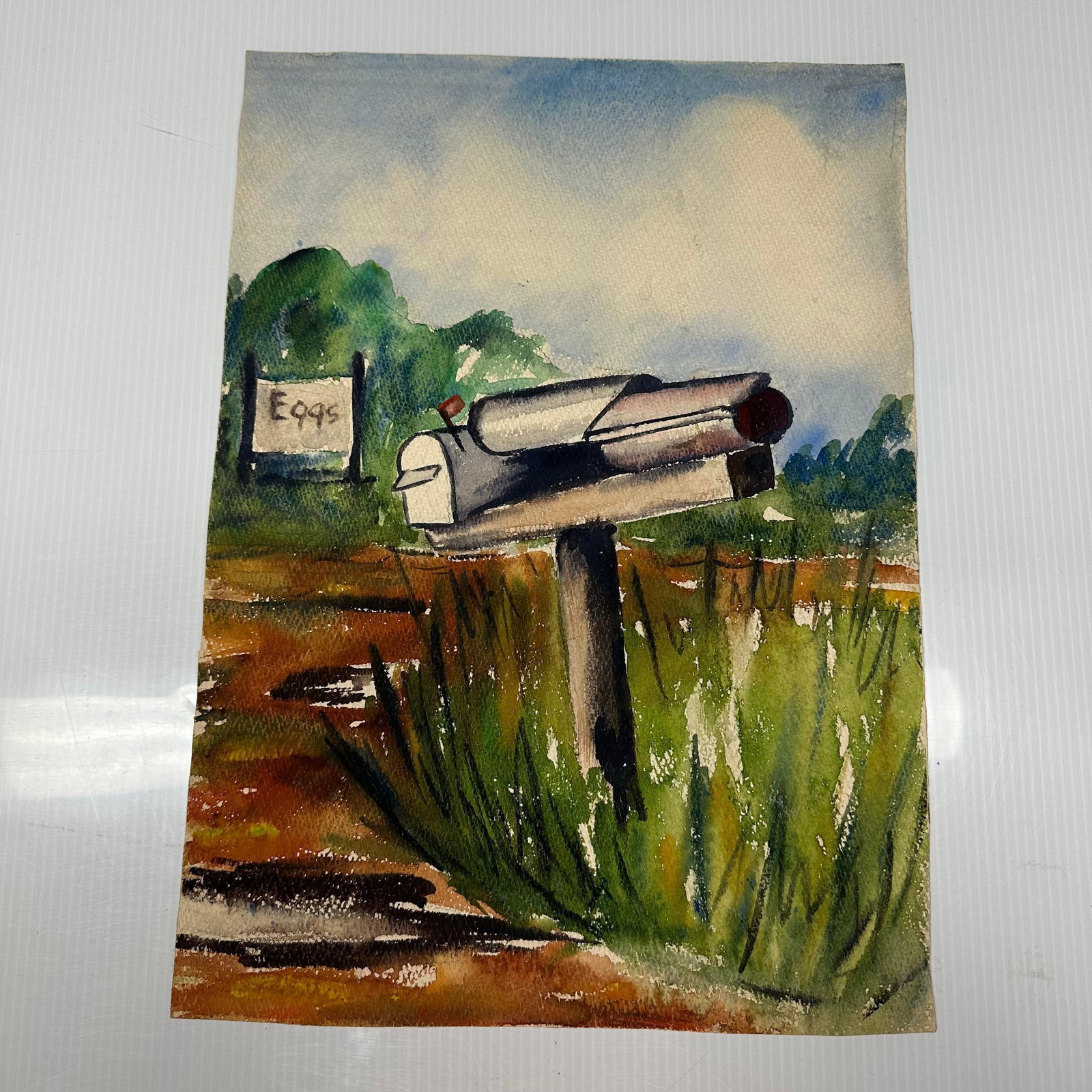 Jo Swanson Mixed Media Painting of Rural Mailbox Landscape: Original mixed media painting on paper depicting a rural roadside scene with a metal mailbox mounted on a wooden post beside tall grass. A small roadside sign reading “Eggs” appears in