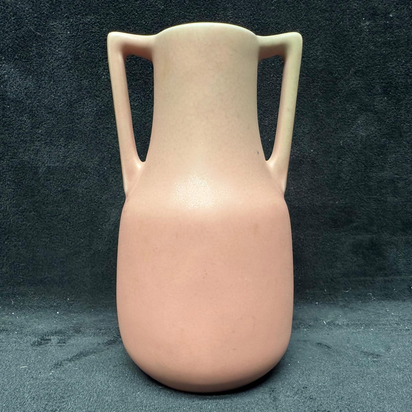 Rookwood Pottery Vase Pink Double Handle Small Vase XXVIII: Decorative ceramic vase featuring a soft pink glazed finish with a double handle. The underside is impressed with a sunburst-style mark and stamped with Roman numerals and numbers, reading XXVIII and 