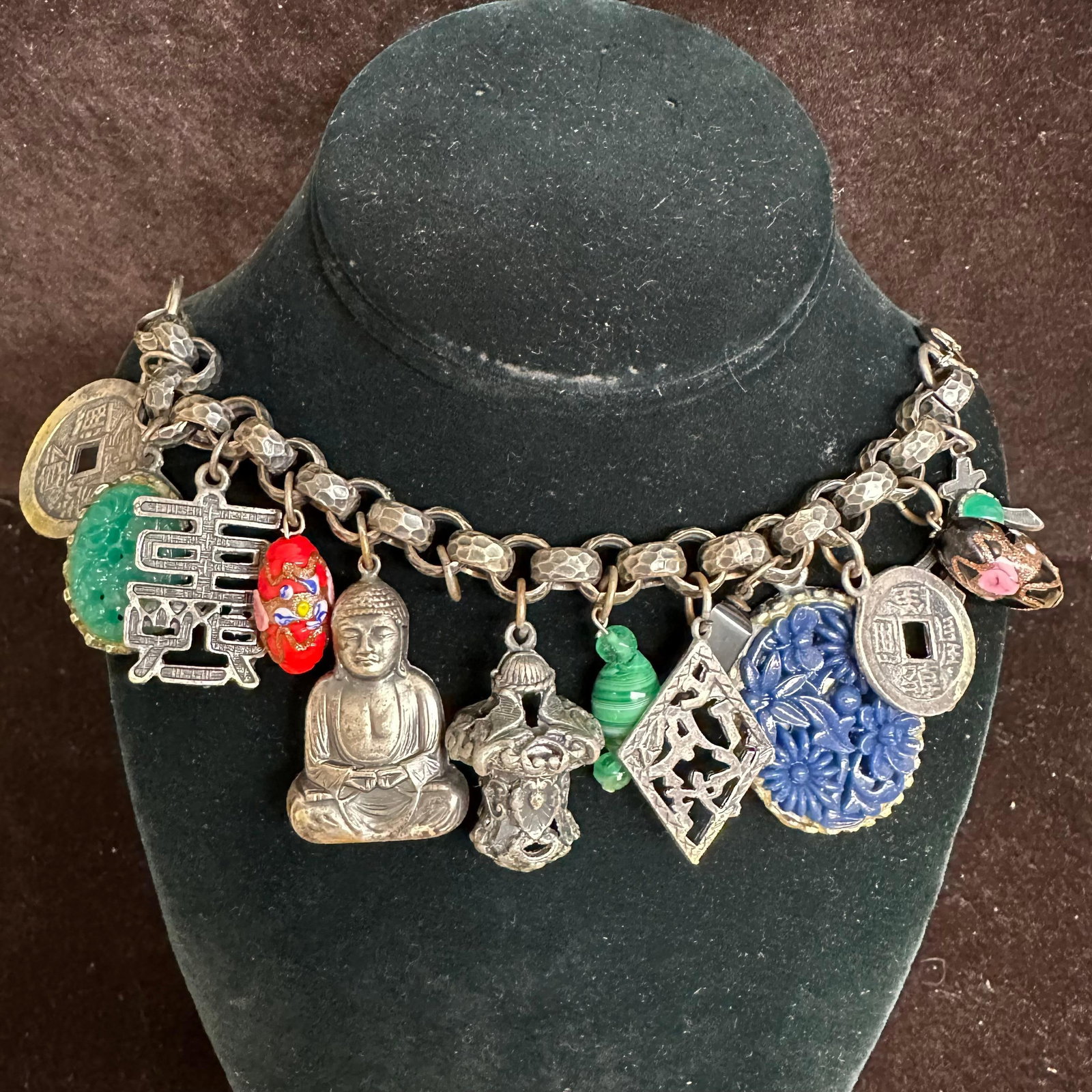 Heavy Multi-Charm Asian-Inspired Statement Bracelet with Coins Buddha and Decorative Pendants Charms: Heavy statement bracelet constructed with a thick hammered-style chain and toggle clasp. The bracelet features multiple dangling charms and pendants with Asian-inspired motifs, including: Chinese-styl