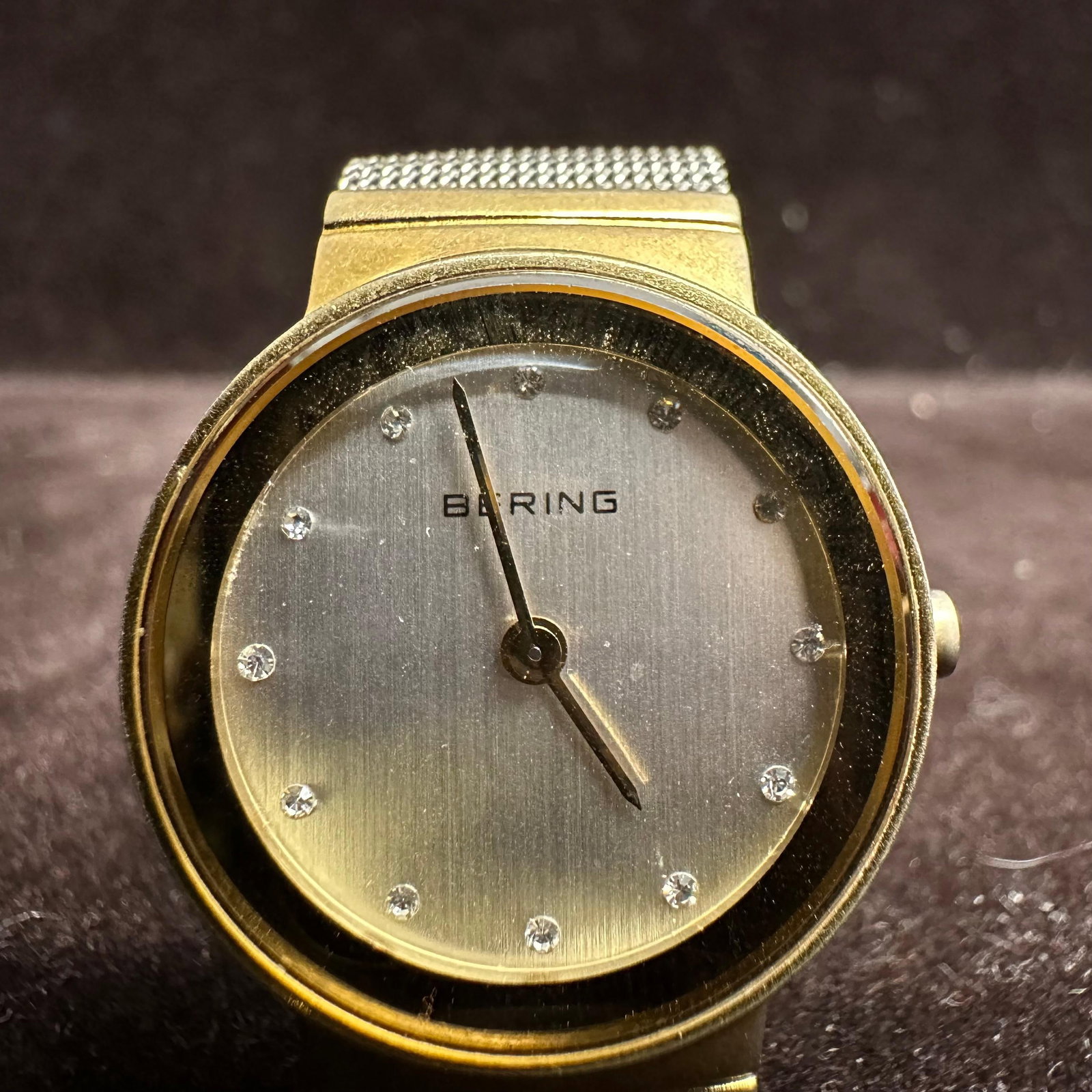 Bering Gold Tone Stainless Steel Wristwatch with Mesh Bracelet: Minimalist Bering wristwatch featuring a gold-tone stainless steel case and silver-tone mesh bracelet. Dial marked BERING with crystal hour markers and two-hand movement. Case back marked stainless