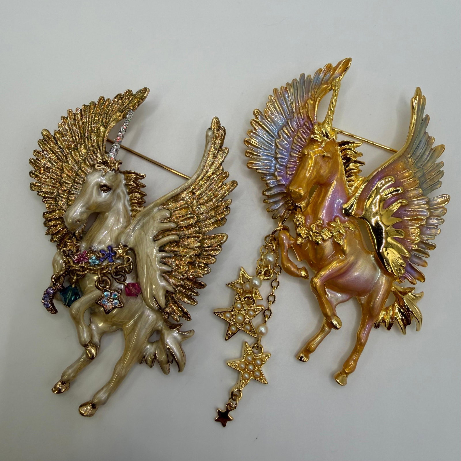 Pair of Kirks Folly Pegasus Unicorn Fantasy Brooches: Matching pair of Kirk's Folly fantasy brooches featuring winged Pegasus unicorns with iridescent enamel finishes and gold-tone accents. One brooch is decorated with colorful charms, while the