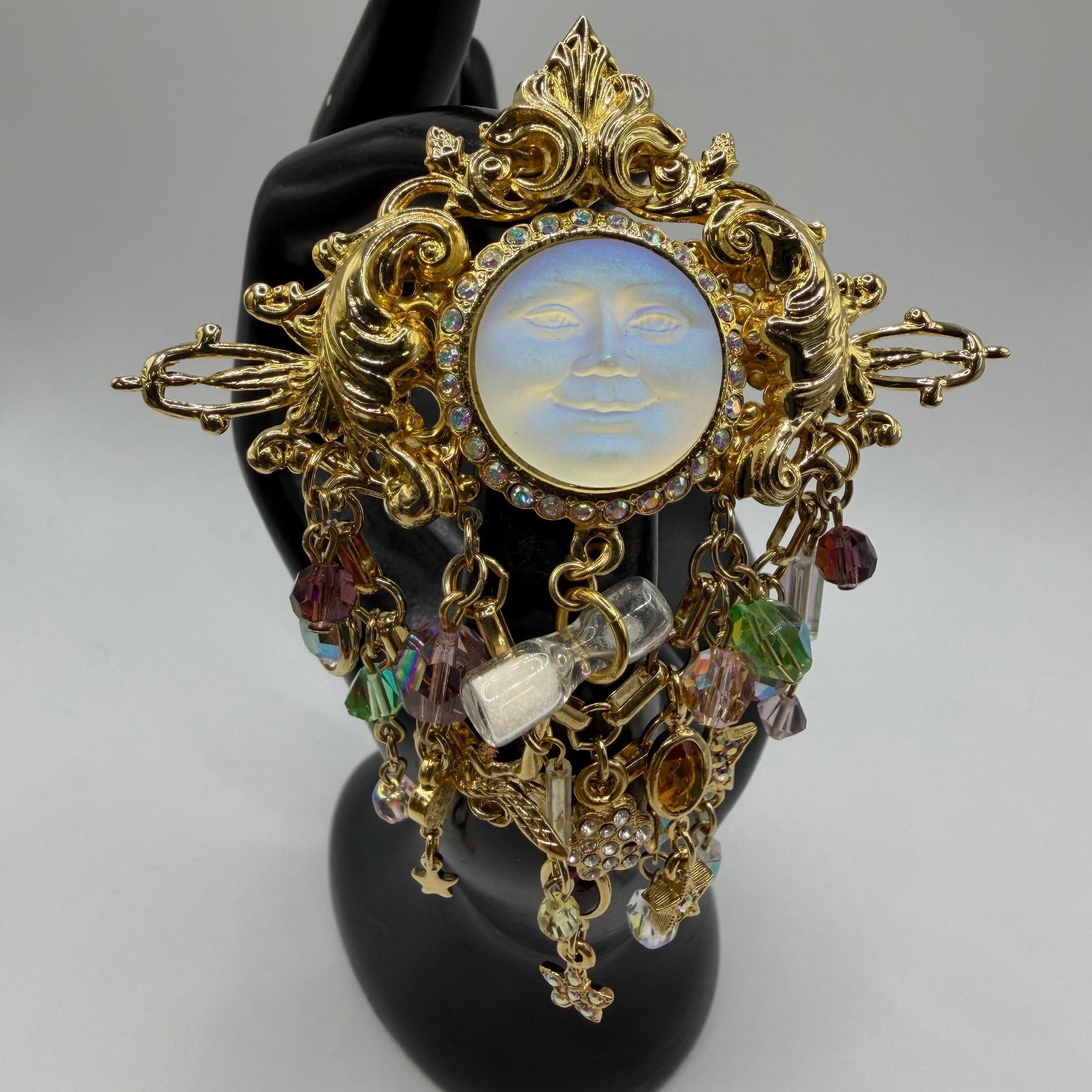 Kirks Folly Pin Seaview Moon Face Signed Mystical Chams Fantasy Brooch: Signed Kirks Folly gold-tone celestial brooch featuring a luminous frosted moon face cabochon framed by aurora borealis rhinestones. The brooch is adorned with cascading celestial-inspired charms