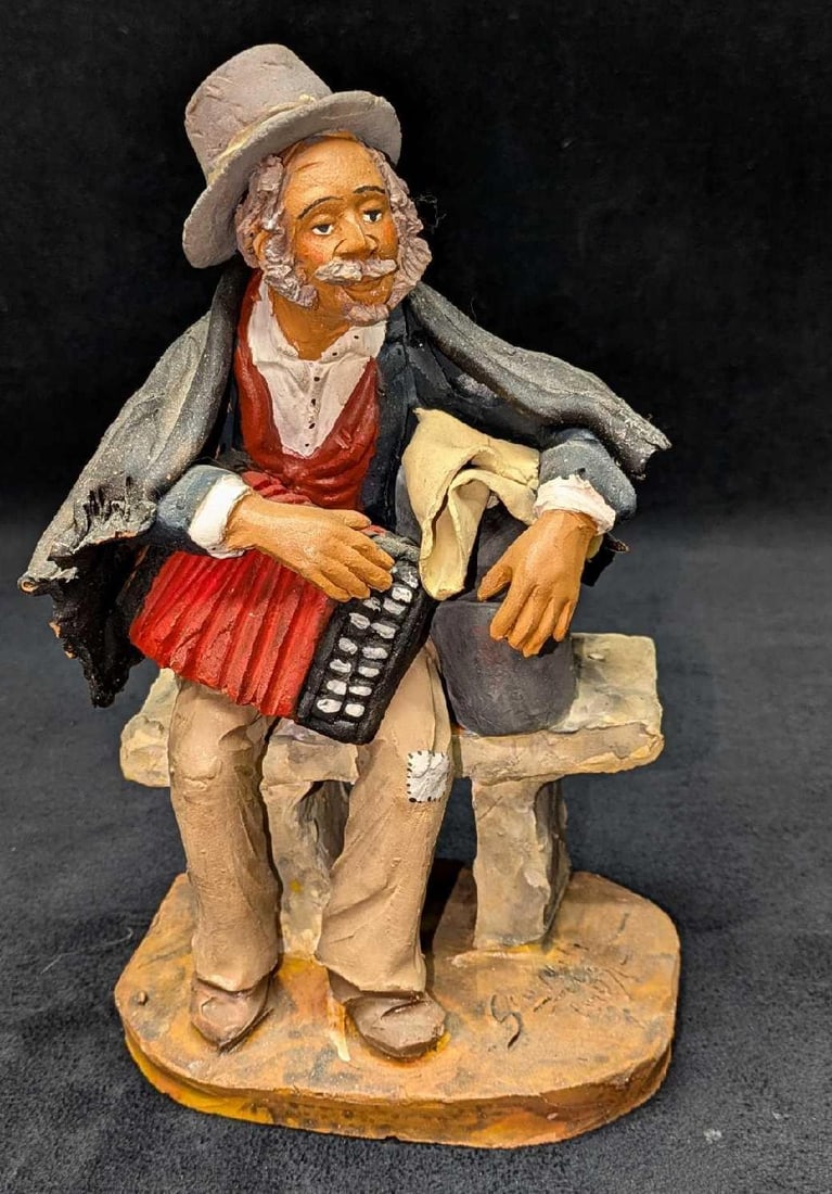Vintage Old Man Accordion Player Sitting On Bench Figurine: Vintage Old Man Accordion Player Sitting On Bench Figurine. Appears to be made of clay/ceramic. This was signed by the artist on the bottom right, but we could not find any information about the