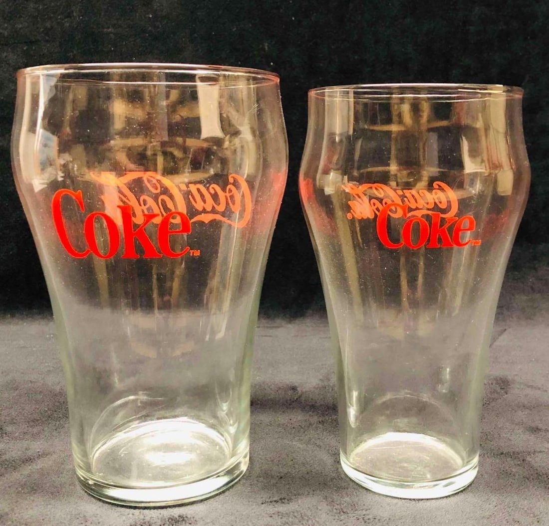 Two Coca-Cola Coke Glasses: This lot contains a Two Coca-Cola Coke Glasses. The large glass is approx 4 1/4" x 4 1/4" x 7" and the small glass is approx 3 1/4" x 3 1/4" x 6 1/2". Together they weigh about 1.4lbs. Overall the
