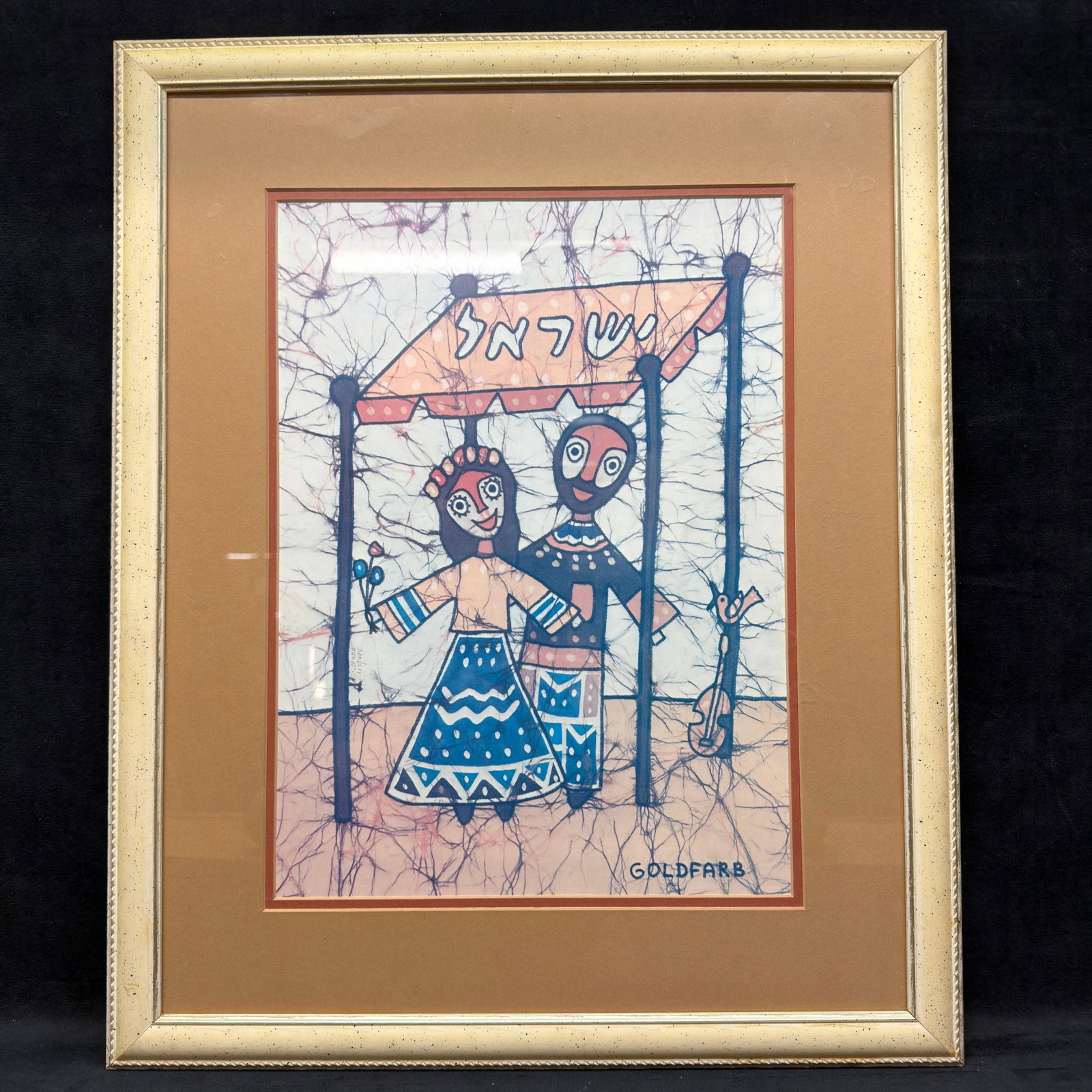 Goldfarb Framed Batik Textile Style Depicting Folk Art Wedding Couple R240: Framed batik textile-style artwork print by Goldfarb depicting a stylized bride and groom standing beneath a wedding canopy with Hebrew lettering above. Print signed GOLDFARB in the lower right. This 