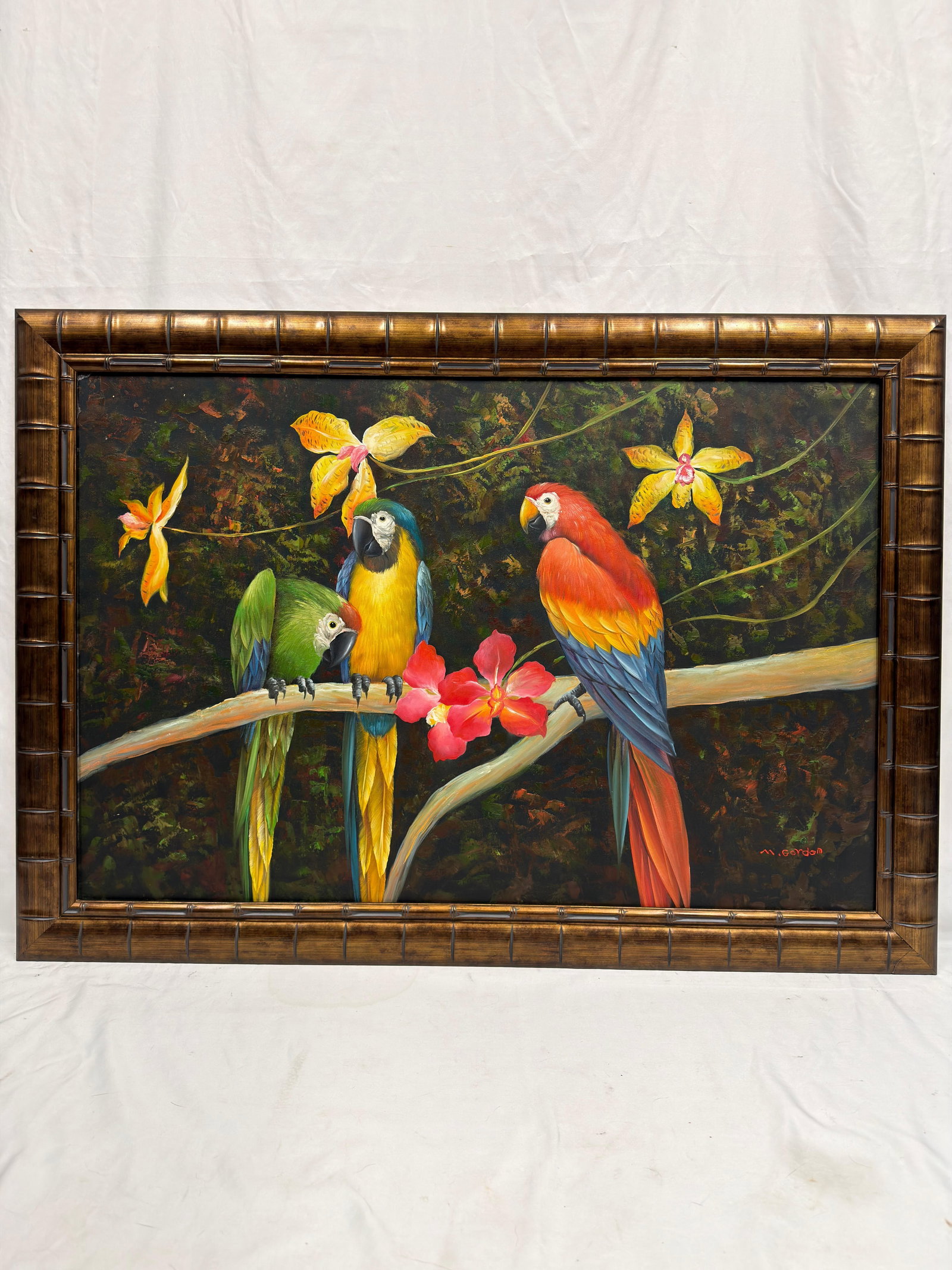 M Gordon Tropical Macaw Parrot Art Painting on Canvas Framed Bamboo Style Border: Colorful art painting on canvas depicting three tropical macaws perched on a tree branch surrounded by orchids and lush rainforest foliage. Signed in red, M. Gordon, at the lower right. Executed in a 