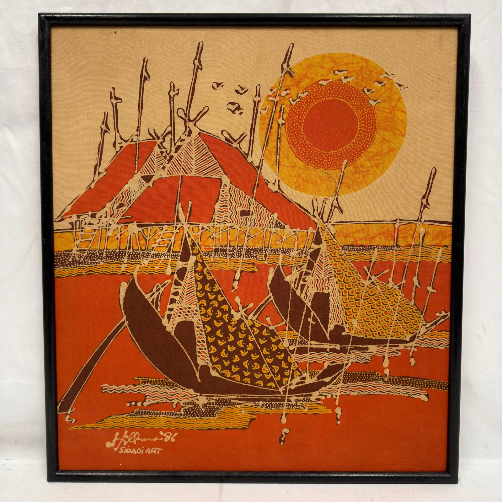 Signed Sioadi Art Batik Textile on Canvas Dated 1988: Original batik textile artwork depicting traditional fishing boats before a stilted village beneath a vibrant setting sun. Executed in warm shades of orange, yellow, brown, and cream, the composition 