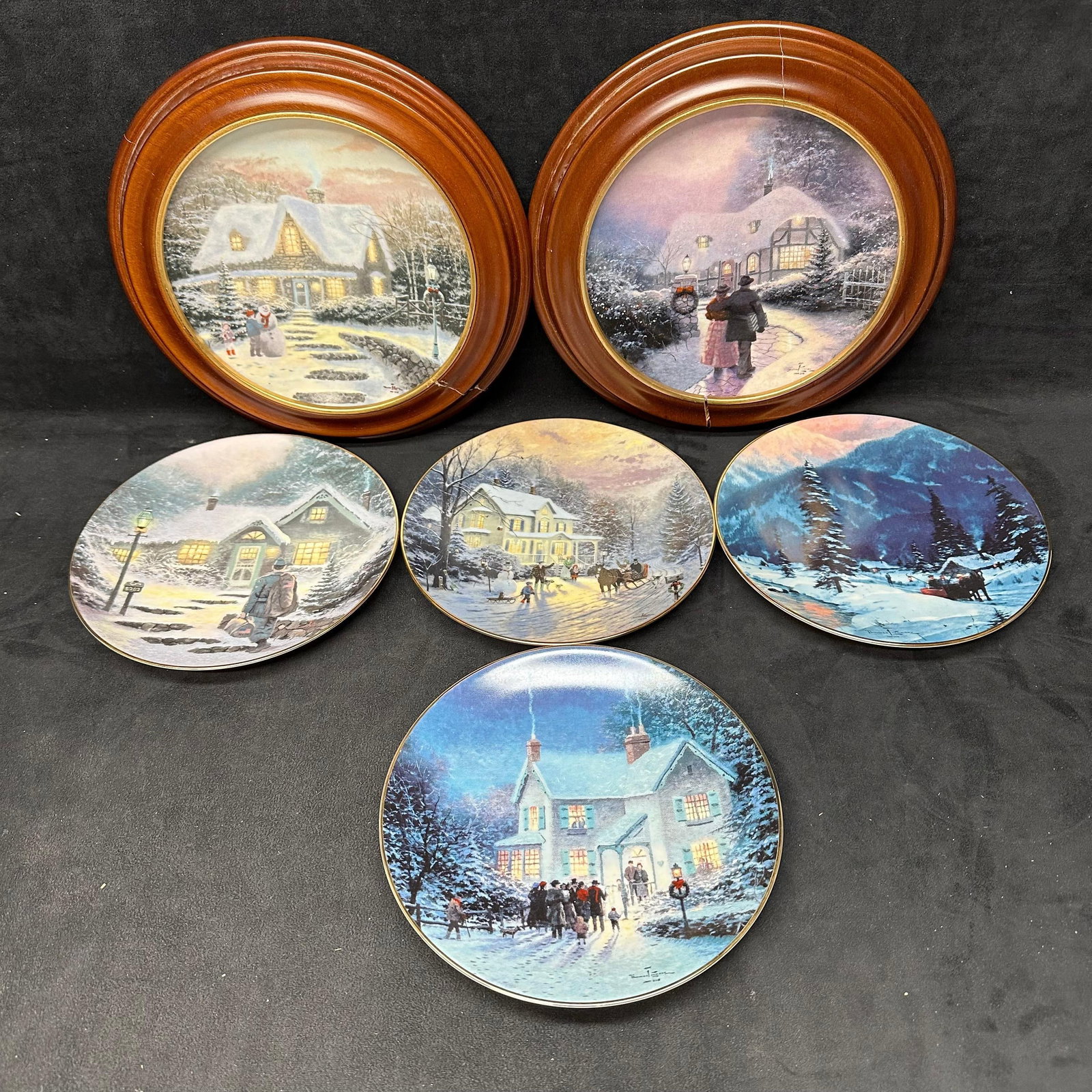 Thomas Kinkade Winter Cottage Holiday Scene Collector Plates Set of Six: Group of six decorative collector plates featuring cottage, village, and winter scenes in the style of Thomas Kinkade. Plates display seasonal imagery, including snow-covered villages, illuminated hom