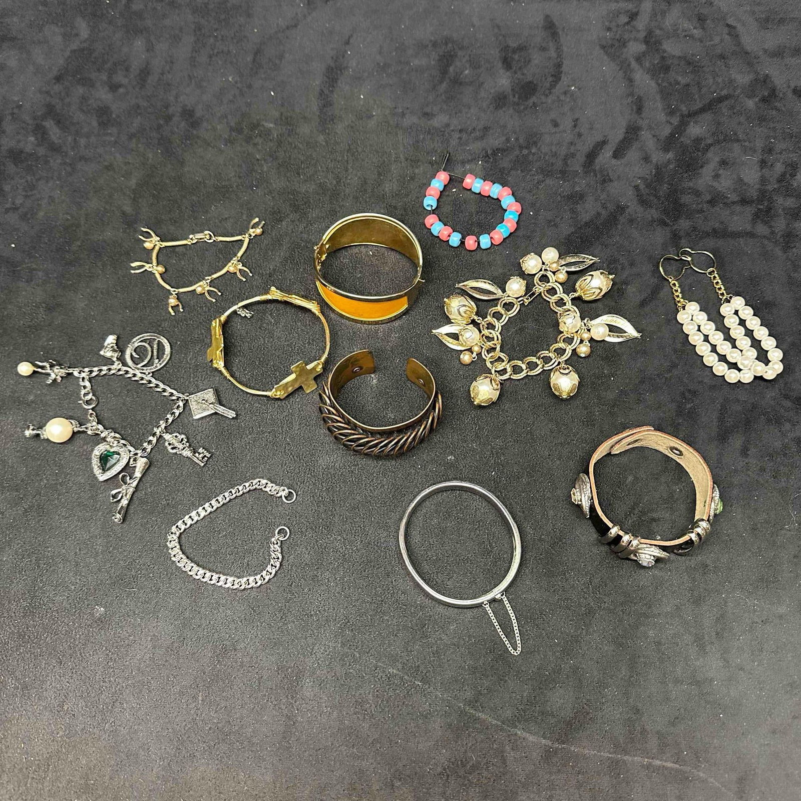 Mixed Costume Jewelry Bracelets and Bangles Lot J15: Assorted vintage jewelry lot including charm bracelet with heart and key charms, gold-tone bangles, cuff bracelets, beaded bracelet, faux pearl settings, plastic beads, and more. Variety of styles and