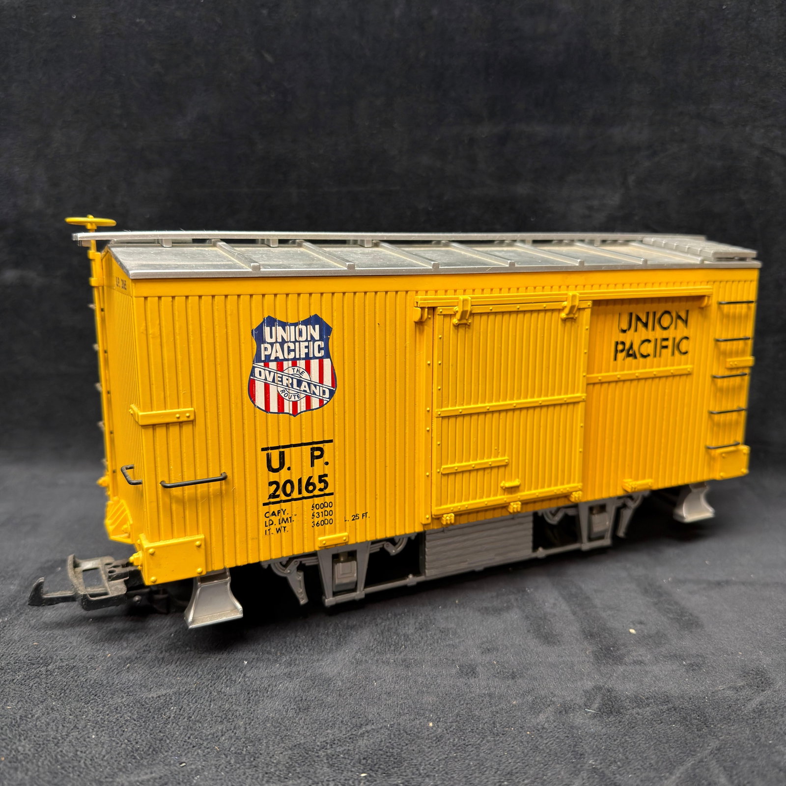 Aristo-Craft Union Pacific G Scale Yellow Boxcar Woodside Style: G-scale Union Pacific Overland Route #20165 boxcar in yellow with silver roof. Features sliding side doors, brake wheel, ladders, plastic wheels, and couplers. Detailed vintage-style Union Pacific gra