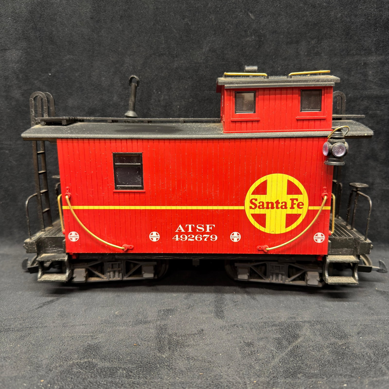 LGB Santa Fe ATSF #492679 G Scale Caboose Red: LGB G scale Santa Fe caboose, road number ATSF 492679. Bright red body with yellow Santa Fe graphics, raised cupola, end platforms, ladders, railings, and detailed trucks. Marked with a label sticker 