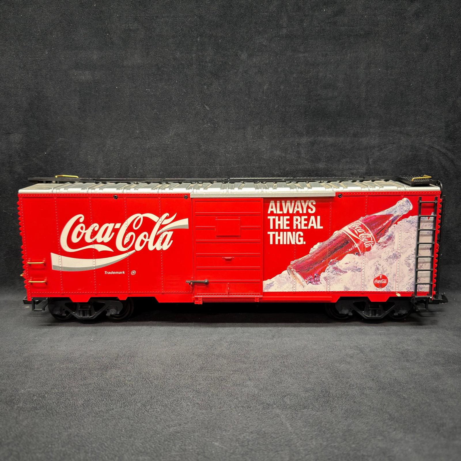 LGB Coca-Cola 25th Anniversary G Scale Boxcar Red: LGB Coca-Cola G scale boxcar featuring red “Always The Real Thing” Coca-Cola graphics with a bottle on ice. Underside bears LGB 25th Anniversary 1968–1993 marking. Sliding side door,