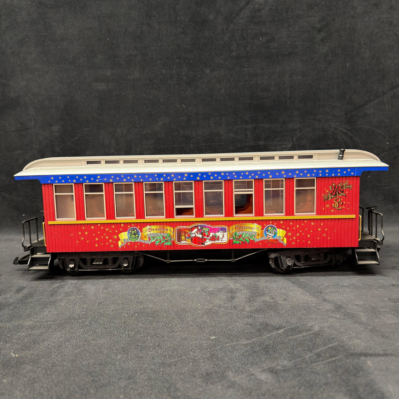 LGB Seasons Greetings Christmas G Scale Old Time Passenger Car: LGB G scale Christmas passenger coach in red with silver roof, blue and gold star trim, and colorful “Seasons Greetings” Santa holiday graphics. Detailed interior seating, plastic wheels, 
