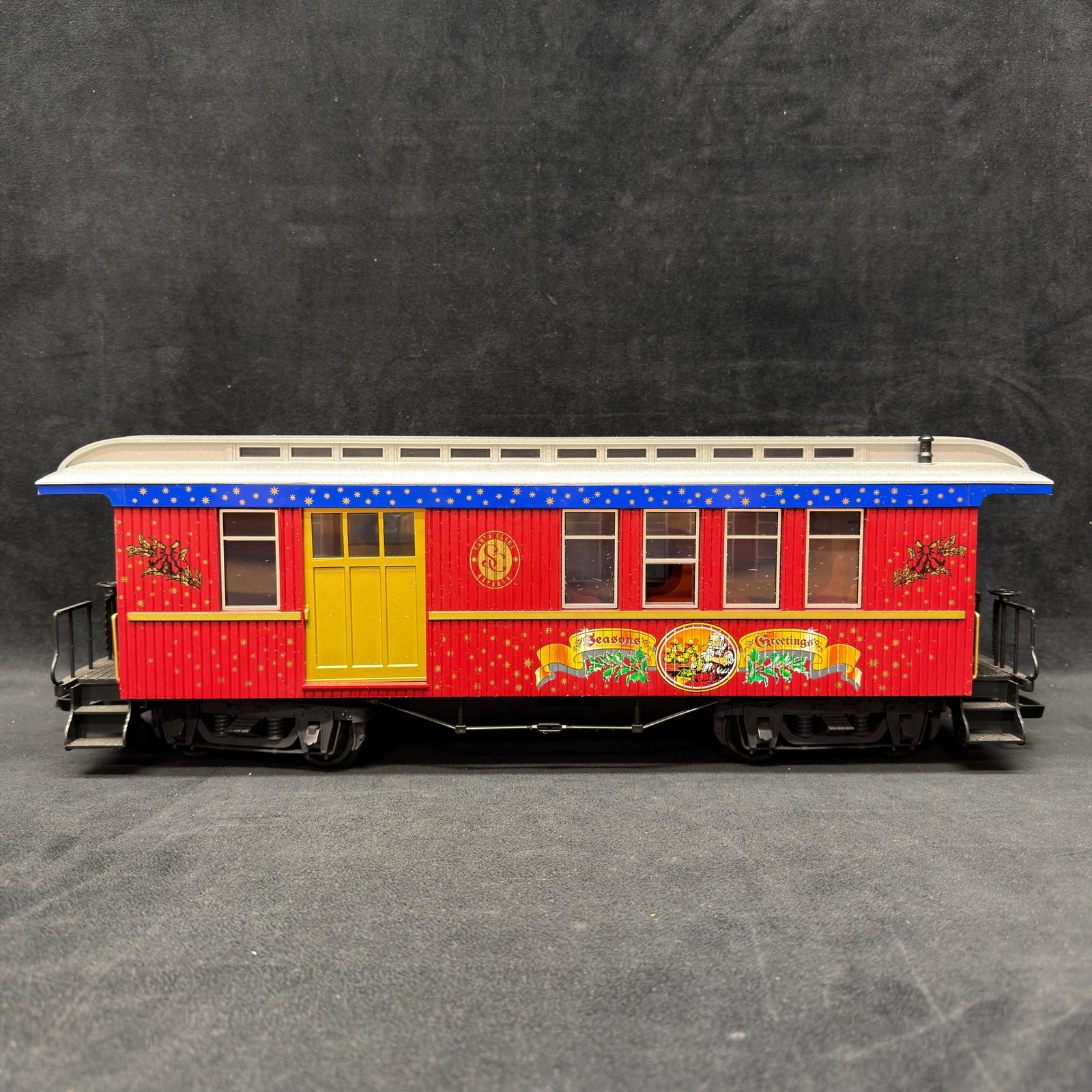 LGB Seasons Greetings Christmas G Scale Passenger Car Red Sliding Doors: LGB G scale Christmas passenger car featuring a red body, silver roof, yellow/gold doors, and colorful “Seasons Greetings” Santa and holly graphics. Marked LGB and Made in China on the und