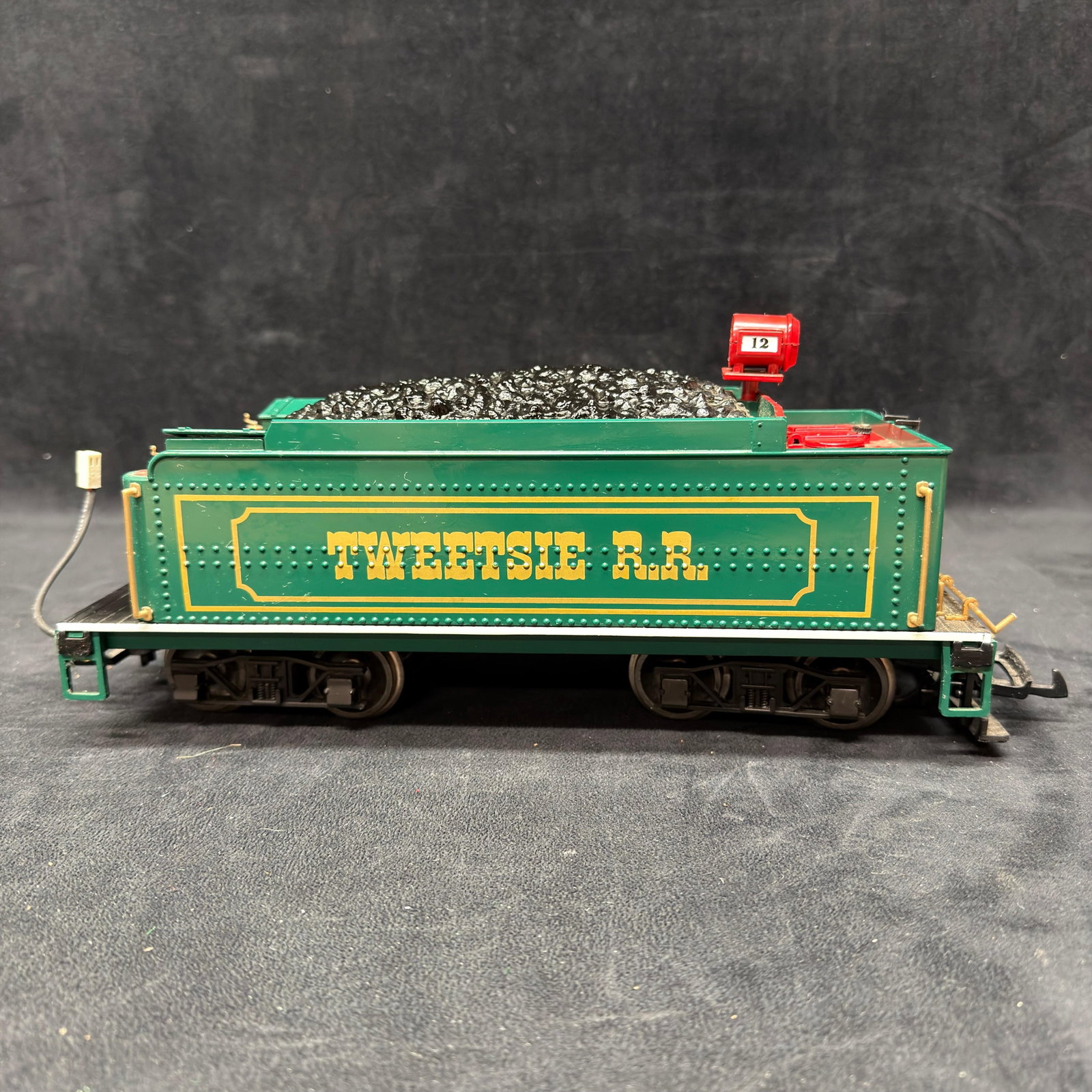 Tweetsie Railroad No. 12 G Scale Coal Tender Train Car: Bachmann G scale coal tender for Tweetsie Railroad locomotive No. 12, finished in green with gold lettering and red details. Features a simulated coal load, metal wheels, and an electrical connector. 