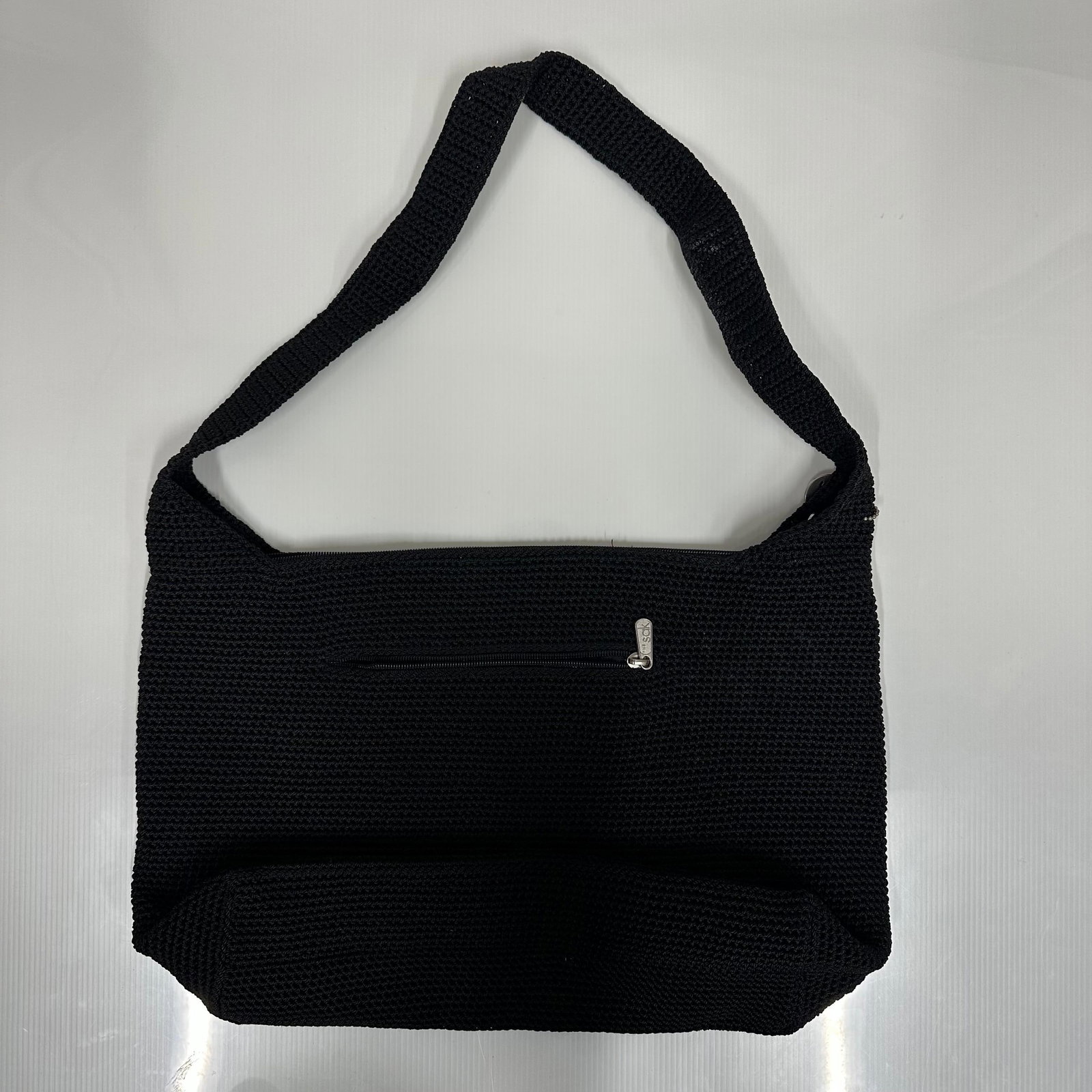 The Sak Black Crochet Shoulder Bag: The Sak black crochet shoulder handbag. Soft woven exterior with a wide shoulder strap. Features a top zip closure and an exterior zip pocket. Silver tone zipper pull marked sak. Interior includes a b