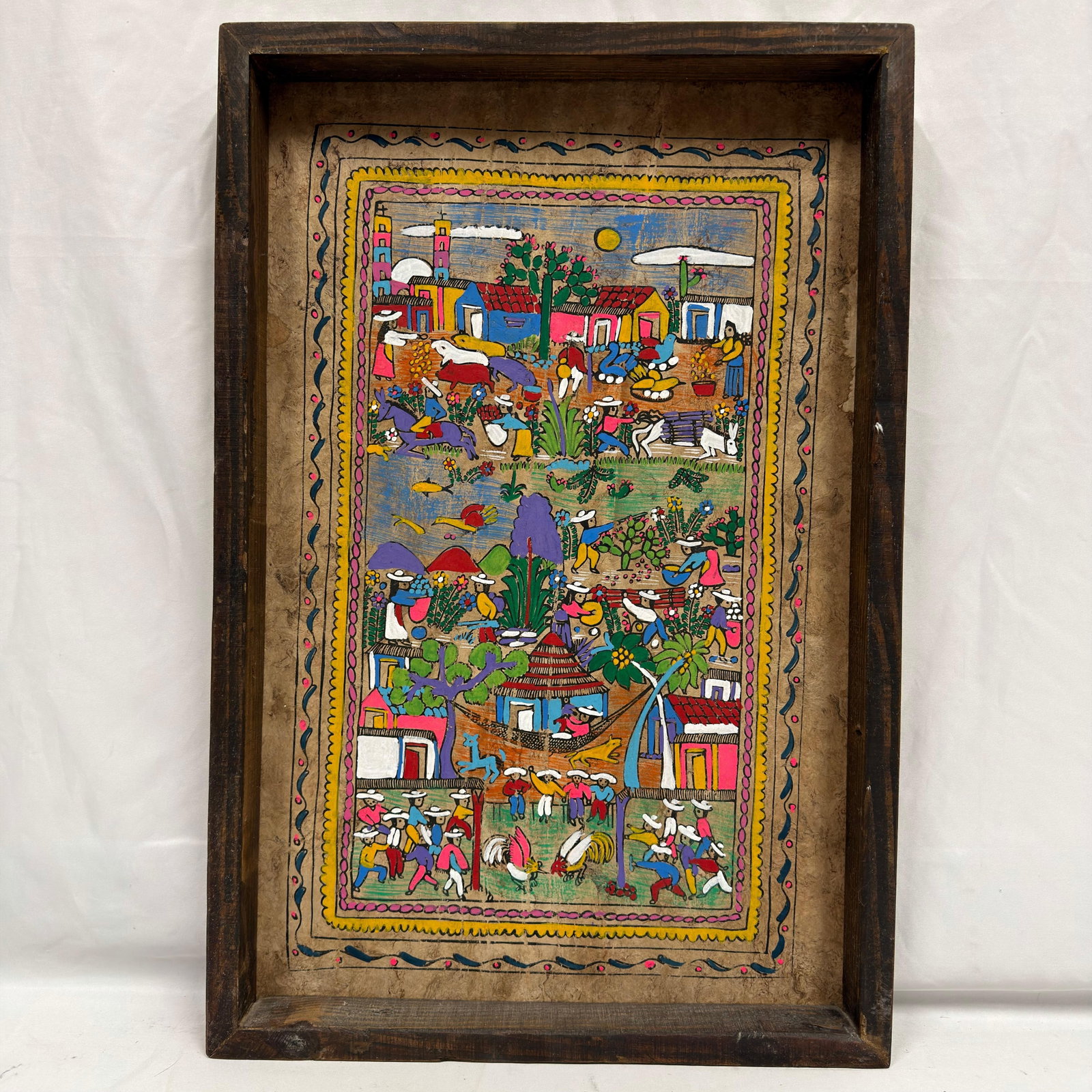 Mexican Folk Art Village Scene Painting on Bark Style Paper: Colorful Mexican folk art painting executed on traditional bark paper, depicting a rural village scene filled with figures, farmers, animals, flowering plants, homes, church towers, mountains, and
