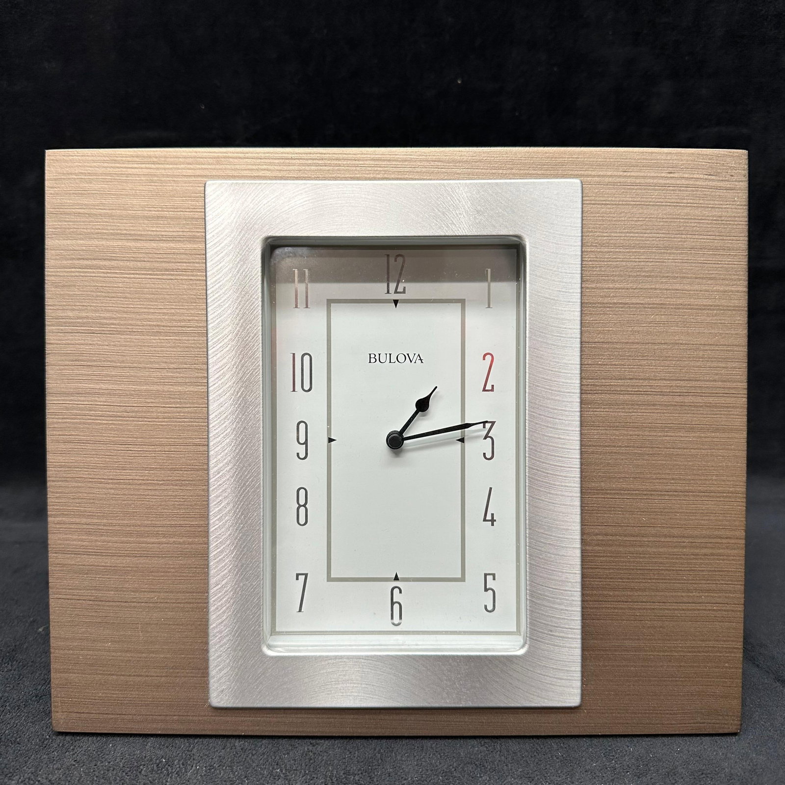 Bulova Quartz Desk Table Clock with Wood Tone Frame: Bulova quartz desk or tabletop clock featuring a rectangular wood-tone frame with a brushed silver-tone inner bezel. White dial with Arabic numerals and black hands. Quartz movement operated by batter