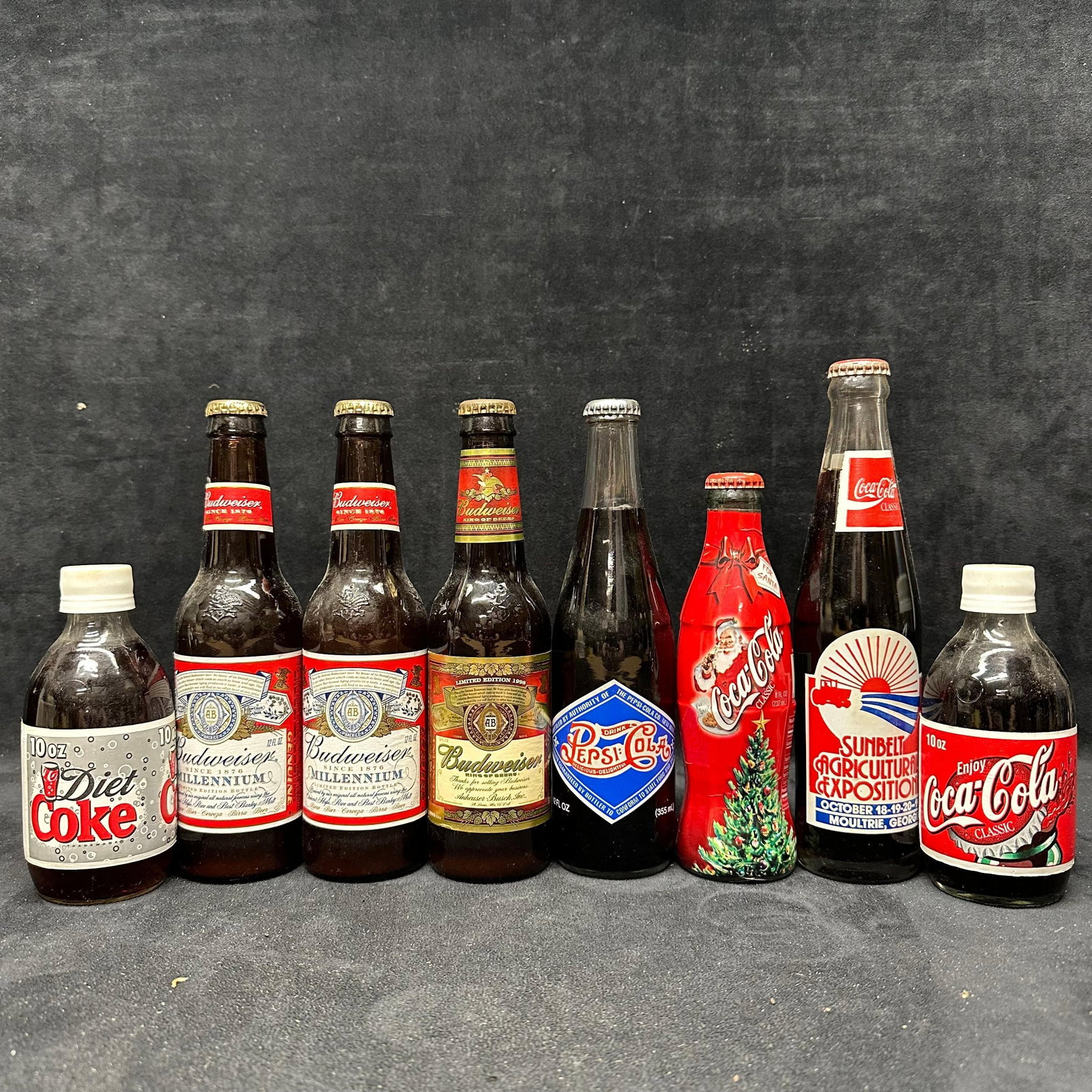 Assorted Vintage Soda and Beer Bottles Coca Cola Pepsi and Budweiser Eight: Group of assorted vintage glass soda and beer bottles, including Coca-Cola, Diet Coke, Pepsi-Cola, and Budweiser examples. Includes commemorative and promotional labels such as holiday, exposition,