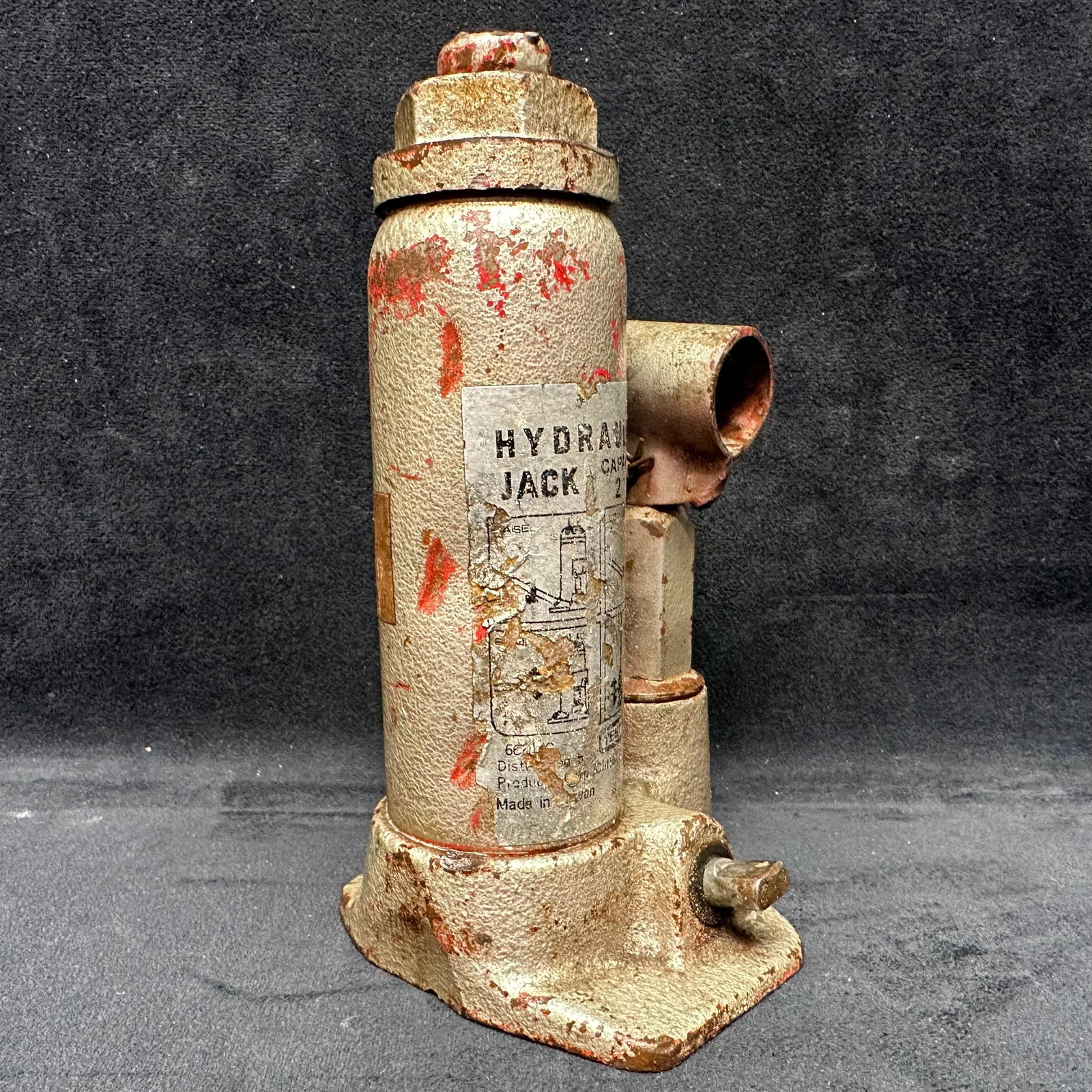 Vintage Hydraulic Bottle Jack 2 Ton Capacity Industrial Tool: Vintage cast metal hydraulic bottle jack with original label indicating 2-ton capacity. Features a side-mounted pump arm socket and a heavy cast base. Shows surface rust, paint loss, wear, and age