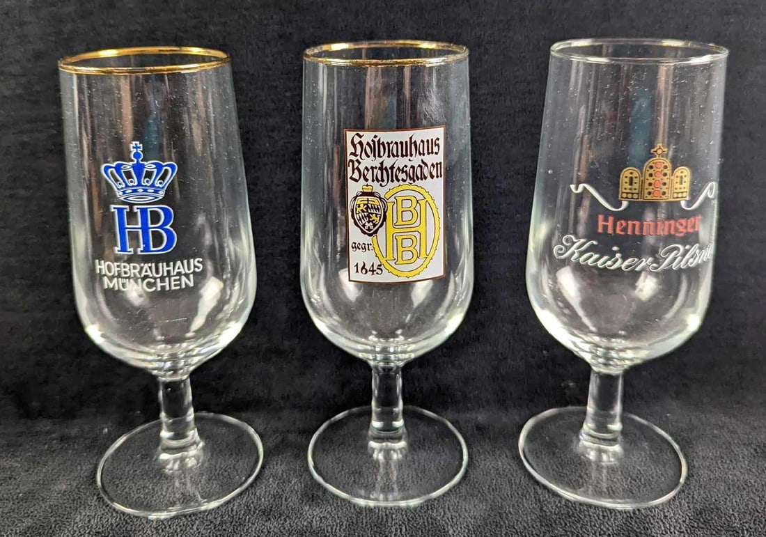 3 Vintage Gold-Rim Stemmed Beer Glasses: This lot includes: (1) Hofbrauhaus Munchen. (1) Henninger Kaiser Pilsner. (1) Hofbrauhaus Berchtesgaden. Each glass is approx 2 1/2" x 2 1/2" x 6 1/2" and together they weigh 1.04lb. The