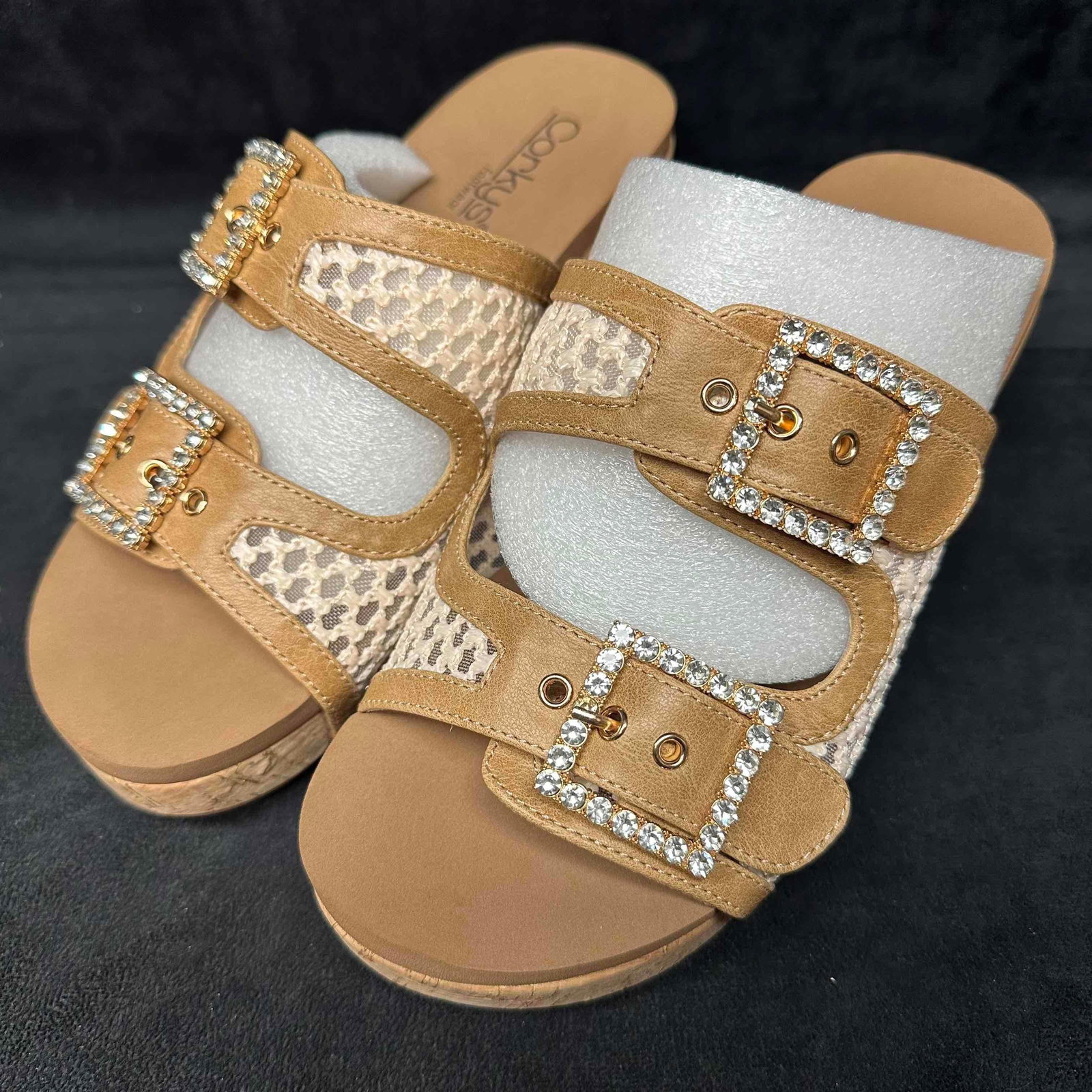 Corkys Footwear Main Squeeze Rhinestone Buckle Wedge Sandals Size 7 Tan: A pair of Corkys “Main Squeeze” wedge sandals, featuring a neutral tan color with textured woven uppers and sparkling rhinestone-encrusted double buckle straps. Designed with a cork-look w