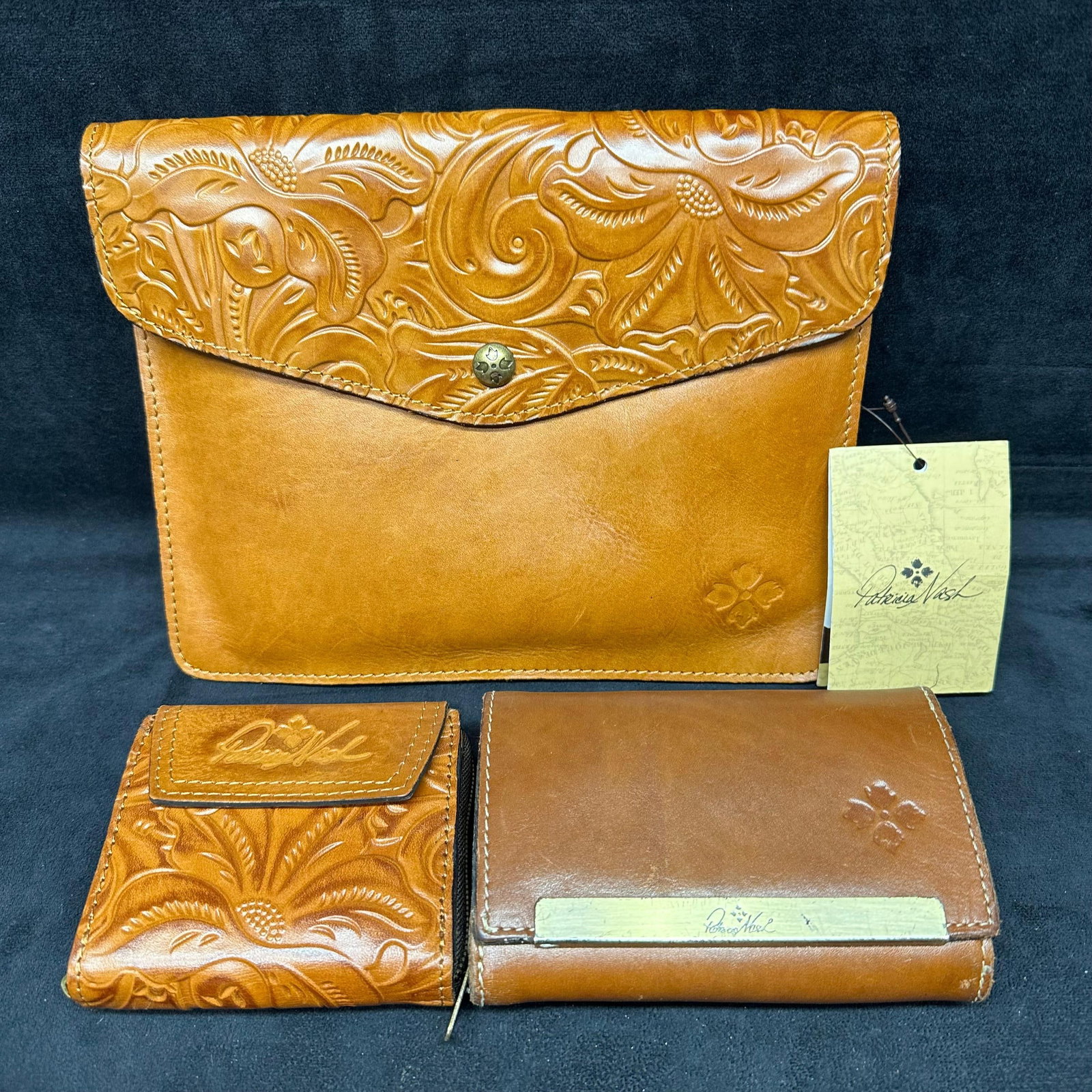 Patricia Nash Tooled Leather Wallets and Clutch Tech Portfolio Set Three Pieces: Collection of three Patricia Nash leather accessories, including two wallets and one clutch tech portfolio. Each piece is crafted from genuine leather with tooled floral designs and embossed