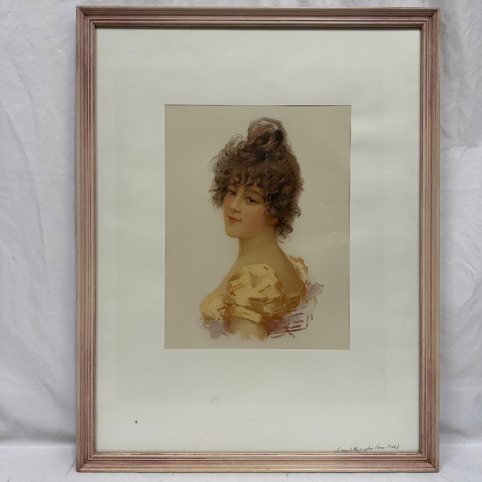 Antique Chromolithograph Portrait of a Woman Circa 1900 Pink Frame: Chromolithograph depicting a young woman with curled hair and a yellow dress, shown in a soft, romantic style typical of early 1900s portrait prints. Presented in a vintage wooden frame with matting. 