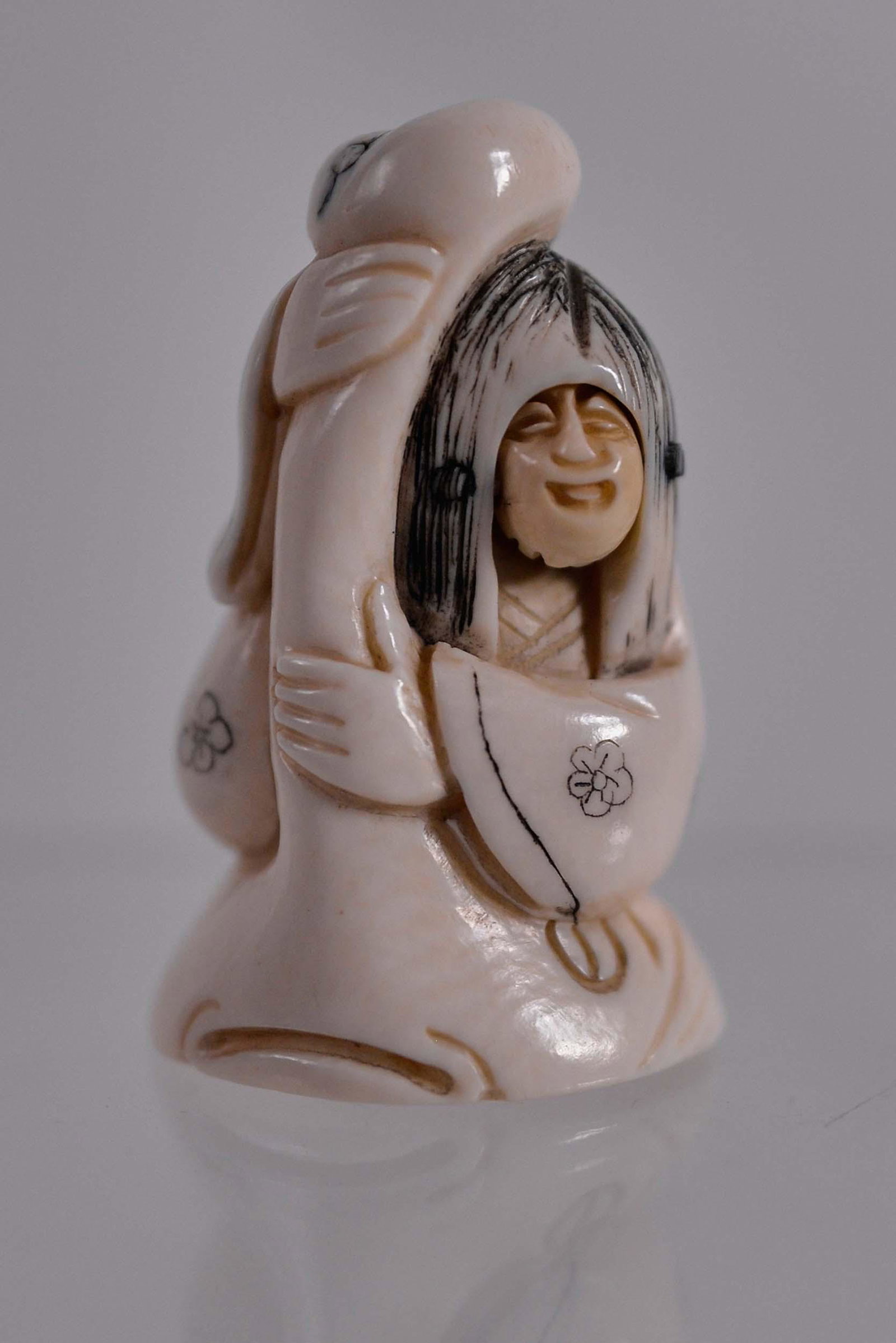 Netsuke seating woman - Début XXème siècle: Netsuke seating woman (Début XXème siècle) Description: Bone netsuke, seated woman with changing face, signature below Dimension (PO): 2" x 1 1/4" x 1" Dimension (CM): 5.08 x 3.17 x 2.54 cm